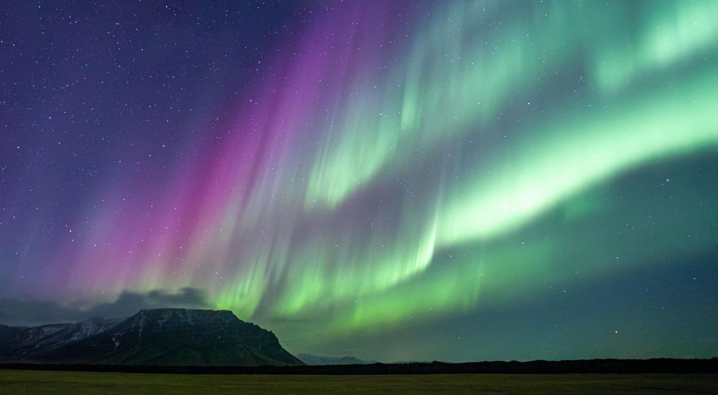 Green and purple aurora borealis over a starry sky, reflecting on a glacial lake with icebergs.