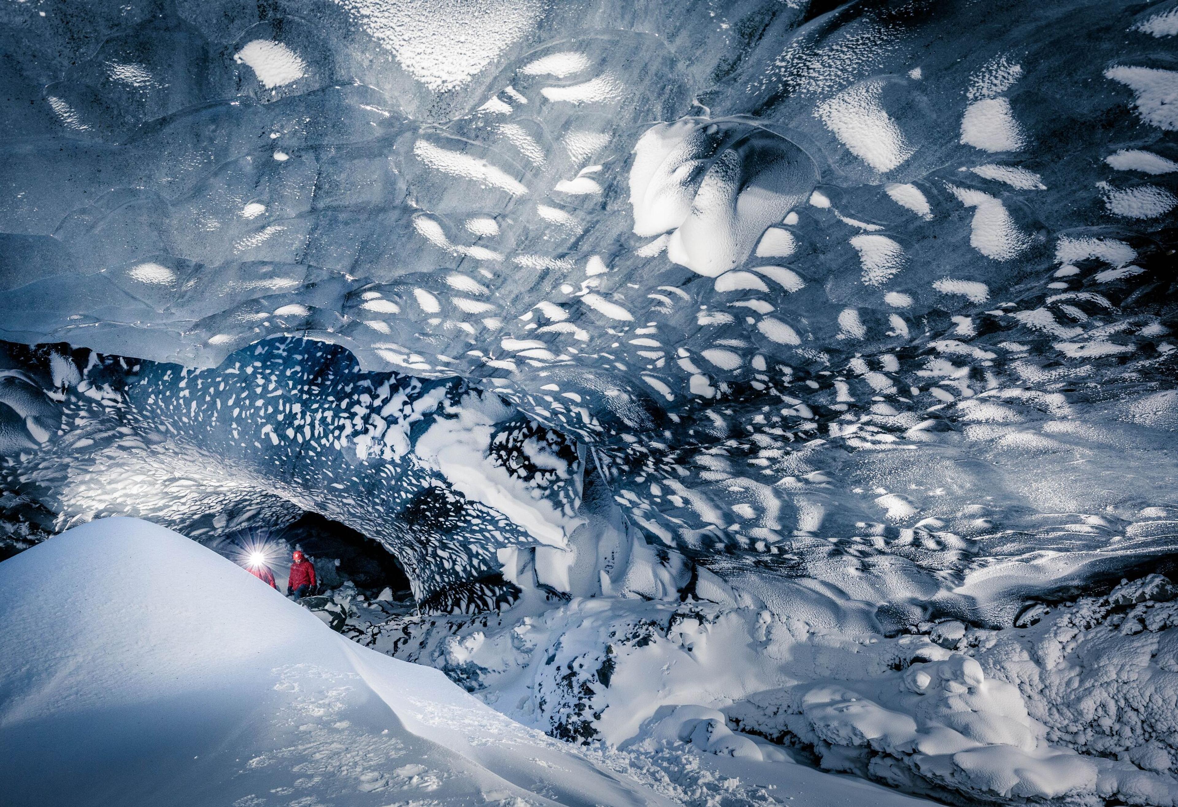 Person exploring inside Mýrdalsjökull glacier ice cave, surrounded by intricate ice formations and deep snow.