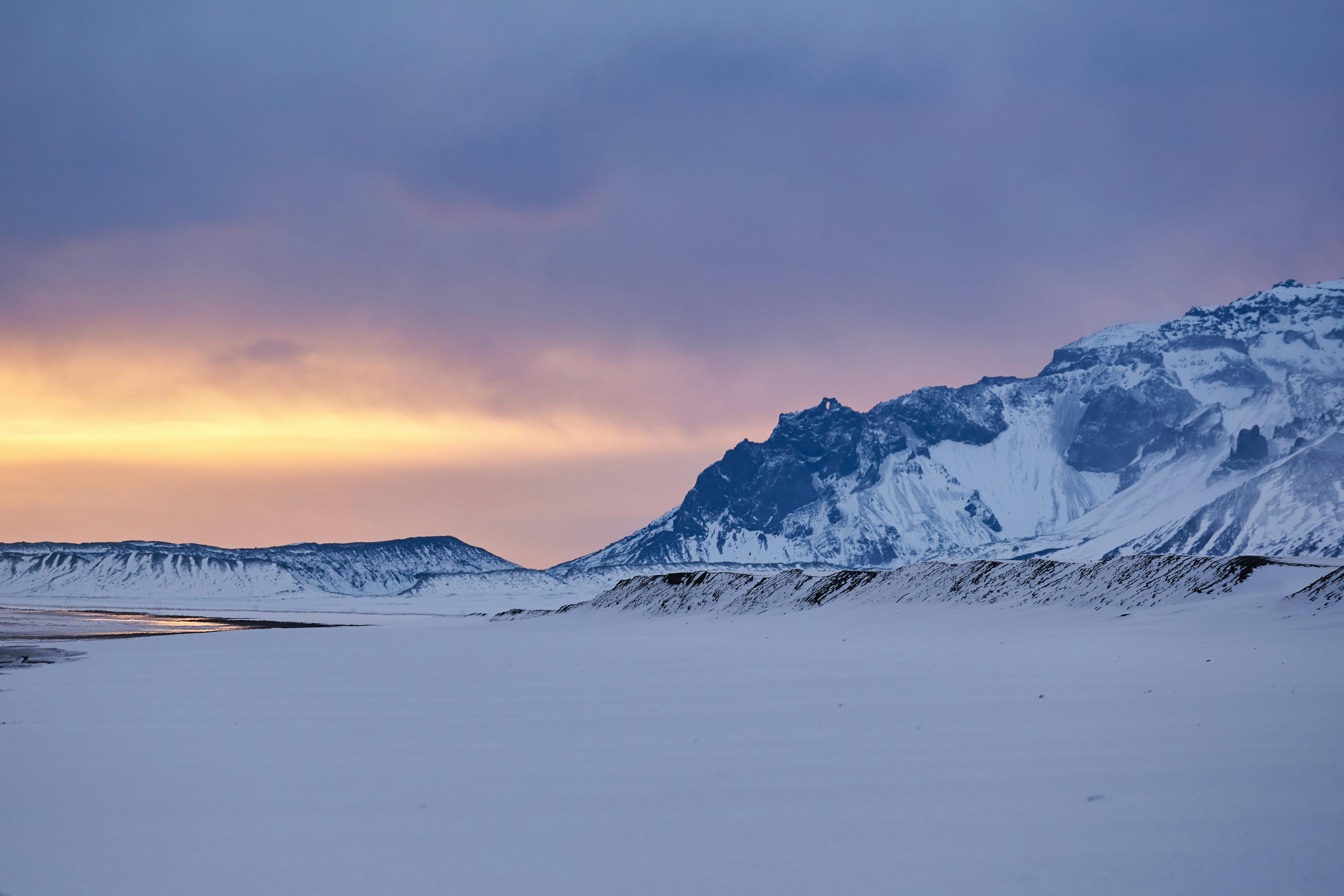 Snow-covered mountain and plain at sunset with pink and orange skies, highlighting the tranquil beauty of the winter landscape.