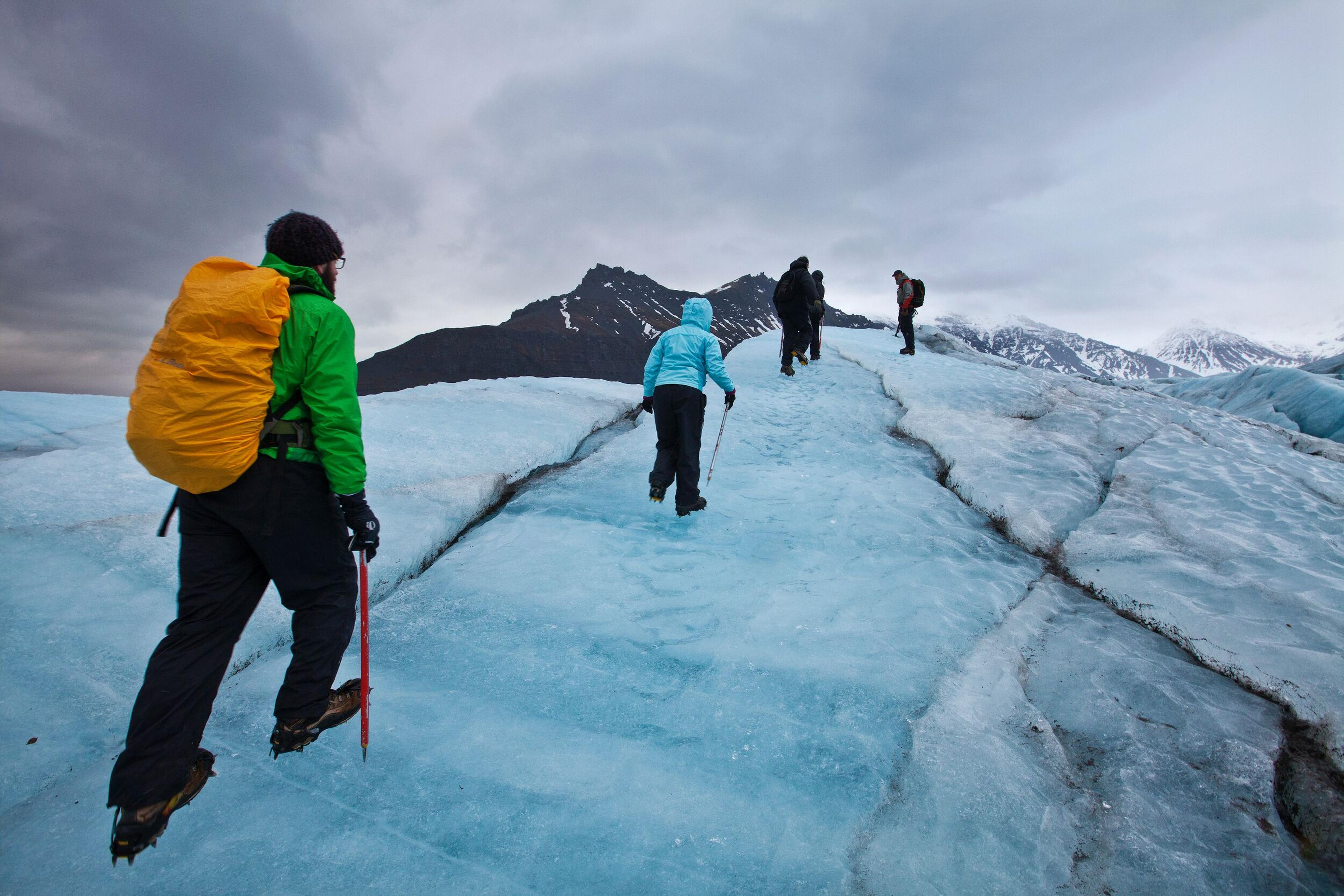 Group of hikers ascending a vivid blue glacier.