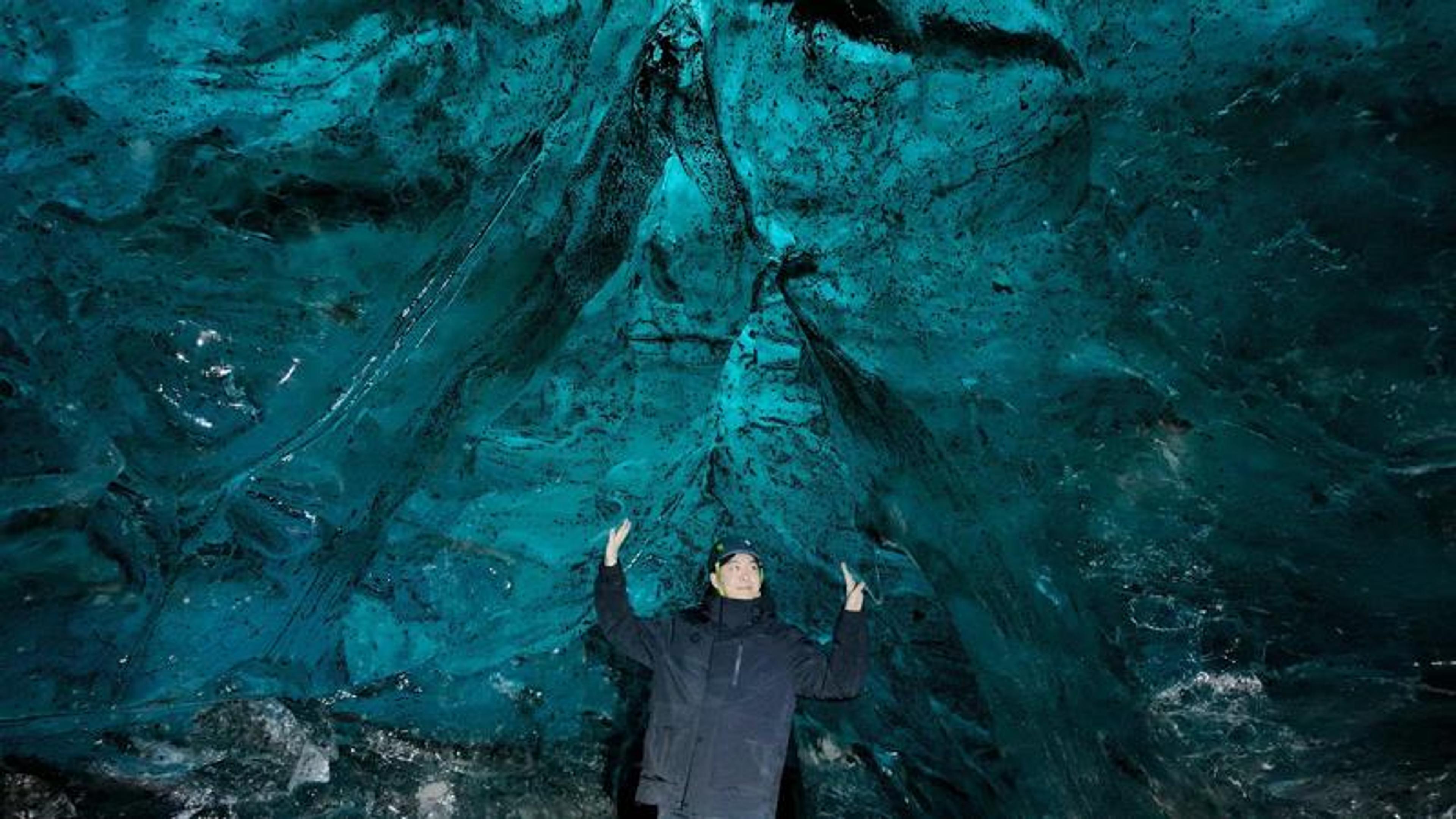 Person with raised hands inside a luminous turquoise ice cave.