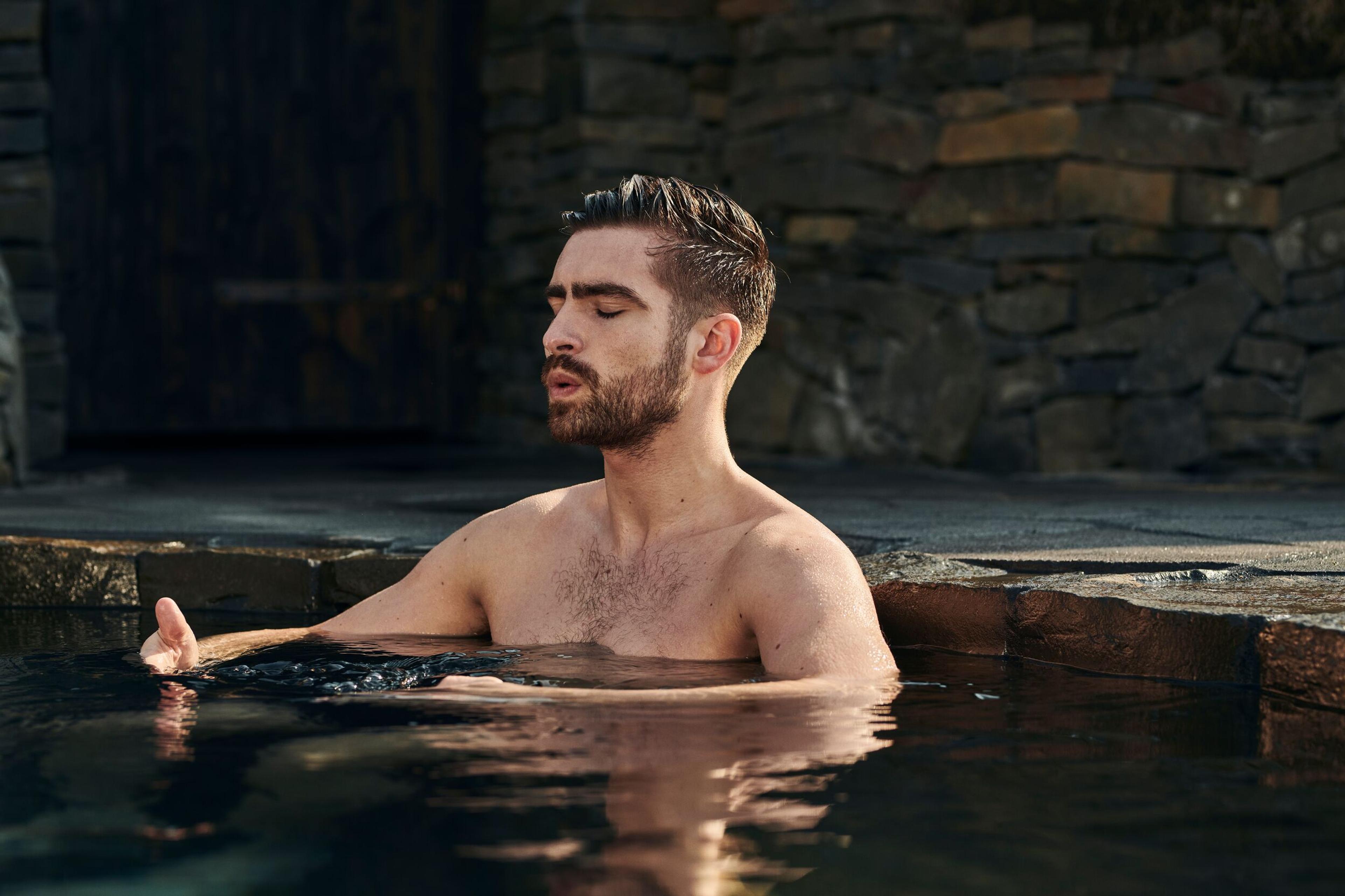 A man relaxing in the cold pool with his eyes closed, against a backdrop of stone walls, embodying a moment of peaceful contemplation.