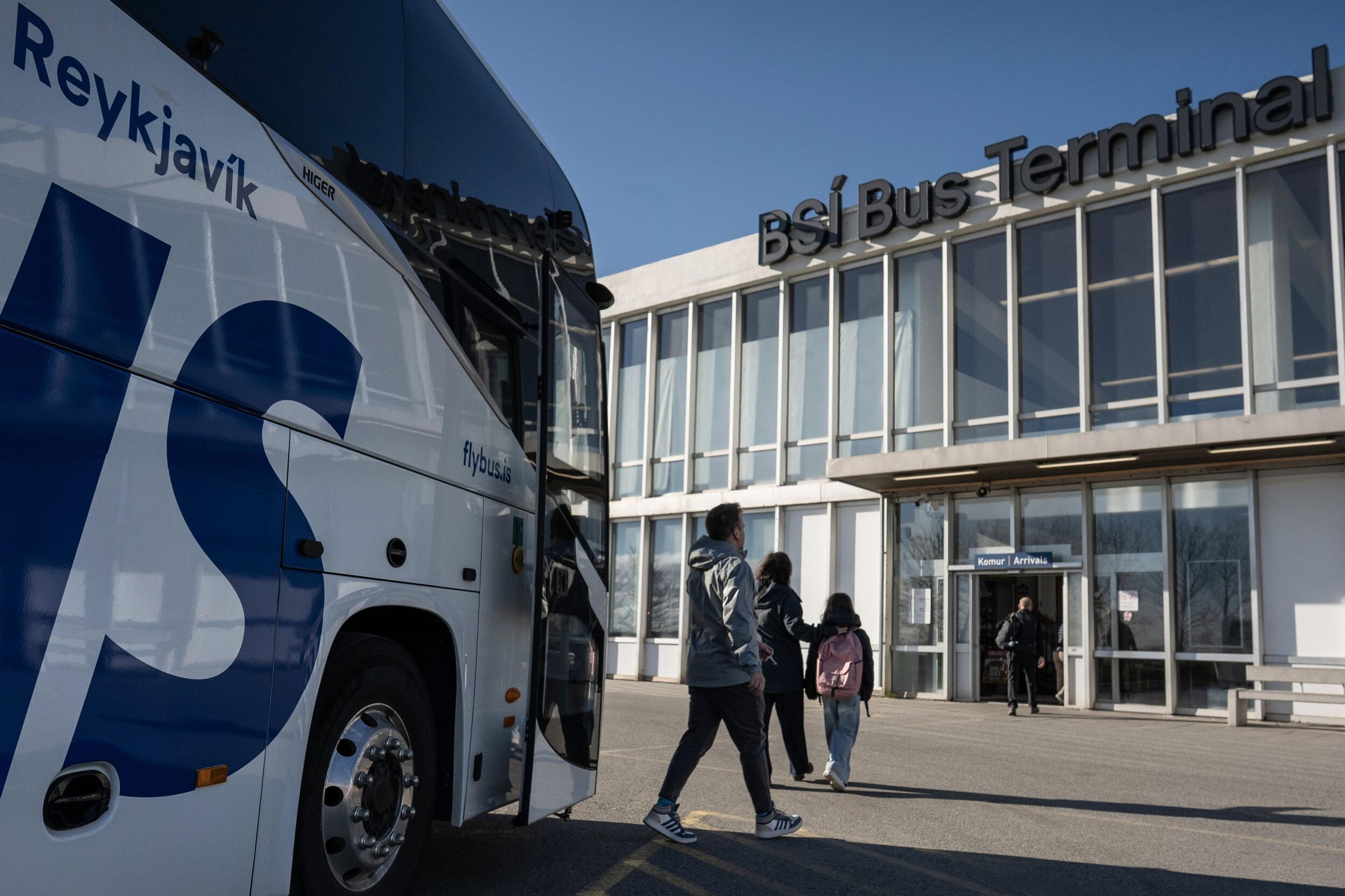 A white Flybus with "Reykjavik" on its side is parked outside the BSI Bus Terminal as people walk towards the entrance.