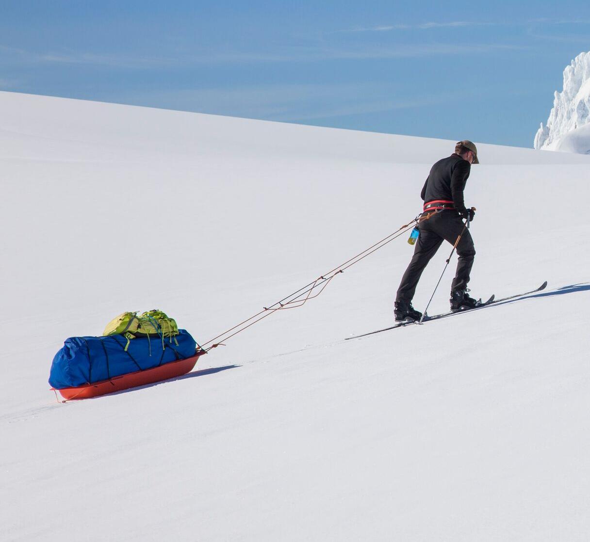 An explorer skying on a glacier carrying gears.