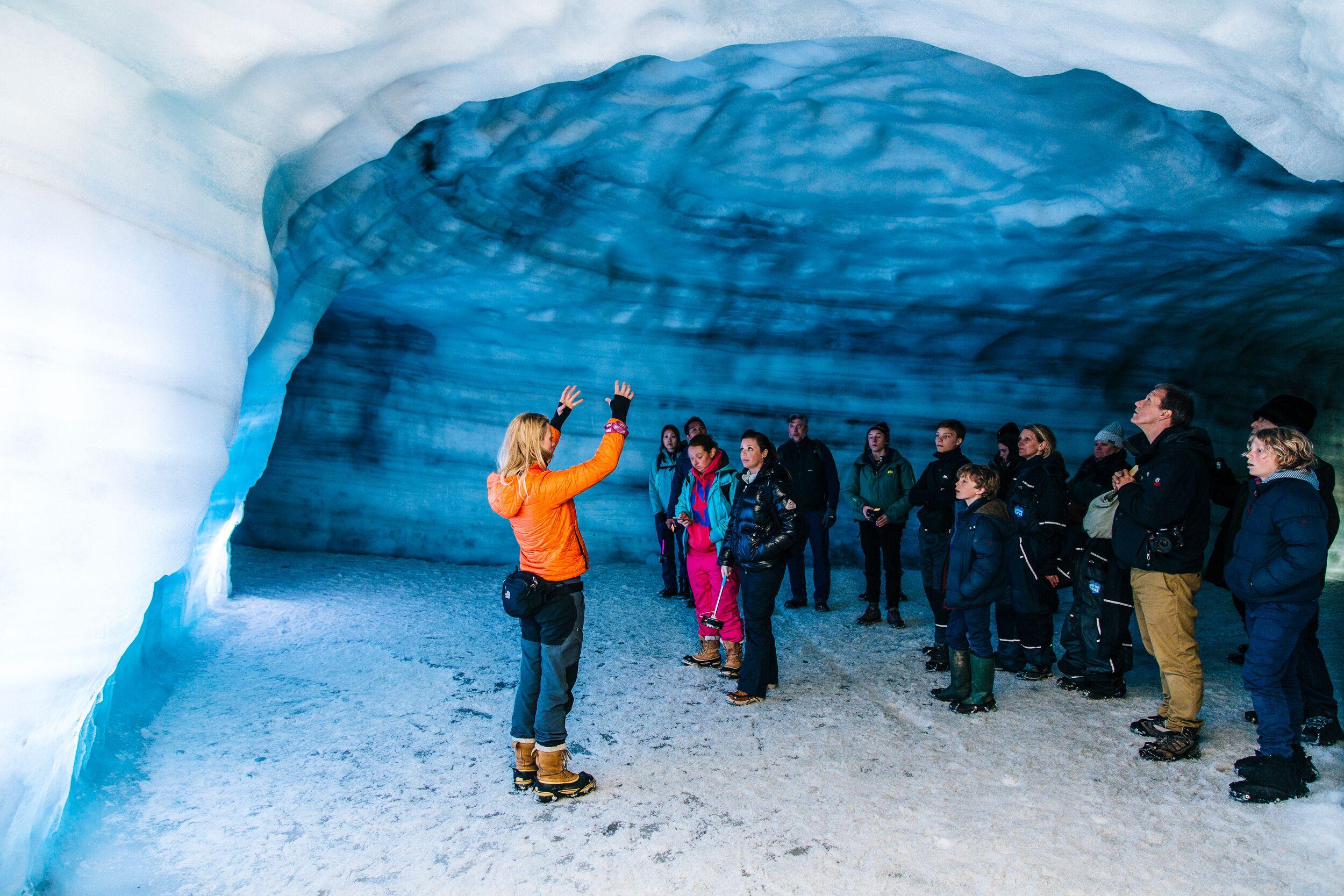 A guide gestures enthusiastically while leading a group tour inside the Langjökull ice cave, surrounded by walls of vivid blue glacial ice.