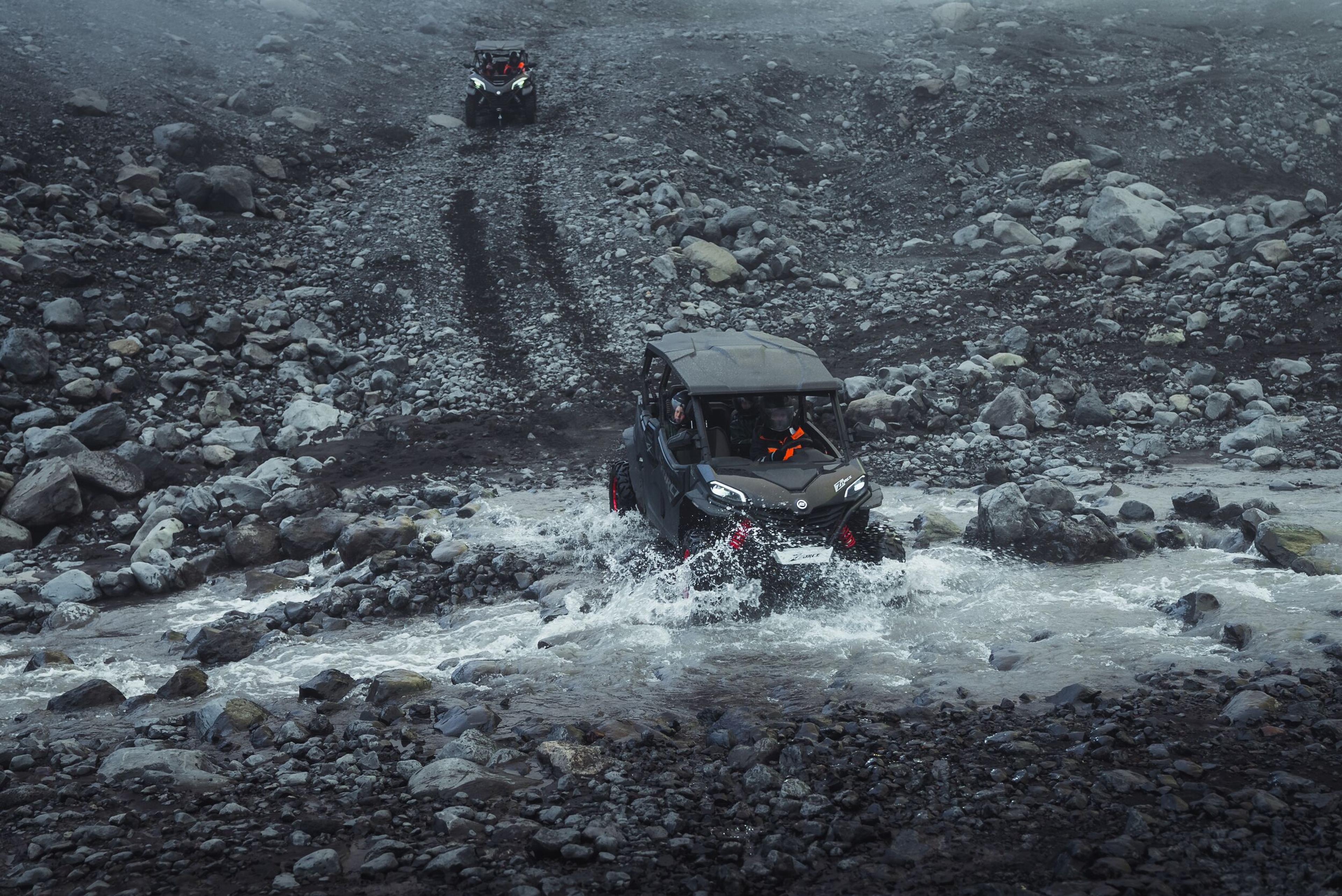 two atvs are driving through a river on a rocky trail .