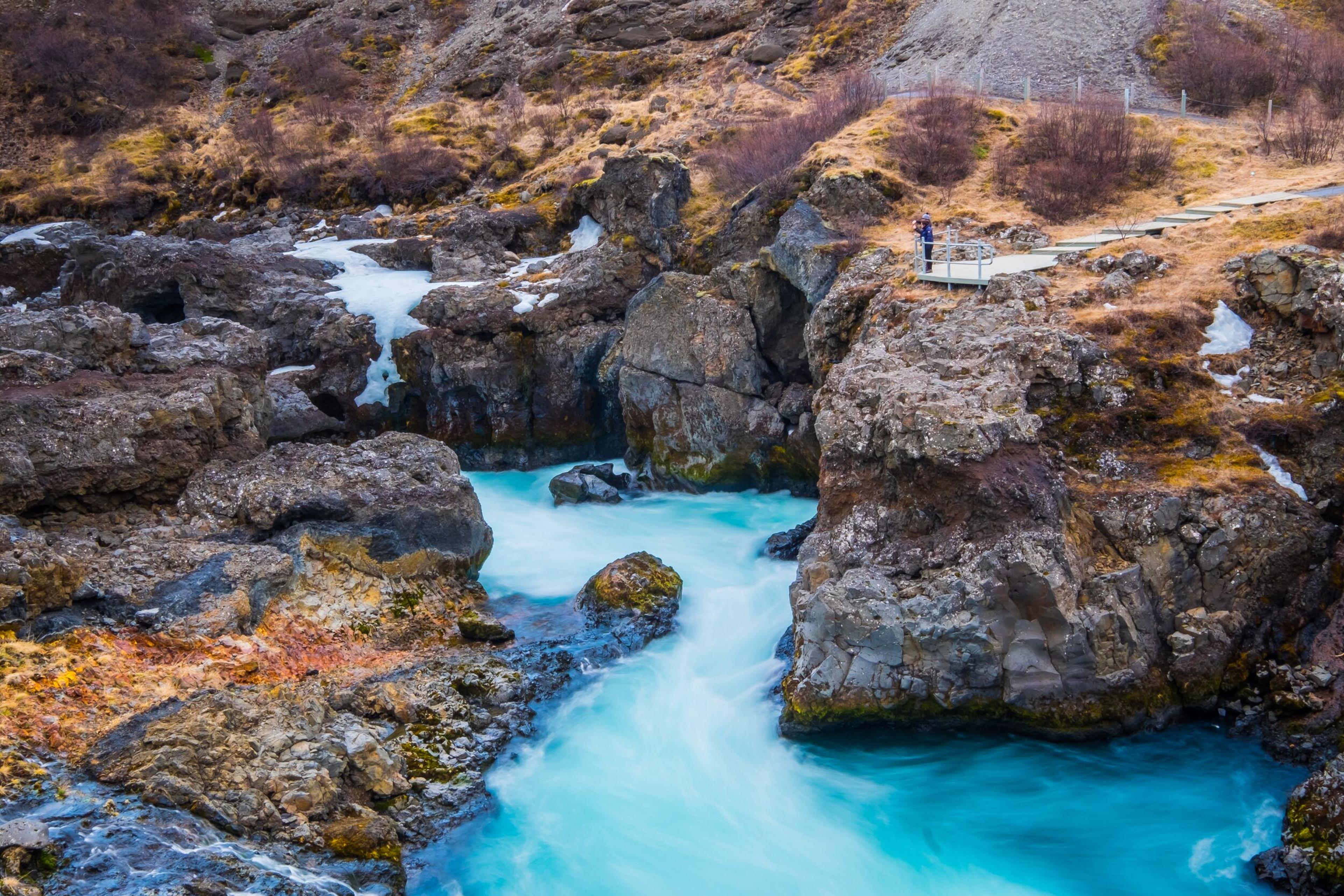 Barnafoss waterfall, showcasing icy rock formations and a vivid blue river winding through a rugged canyon in Iceland.