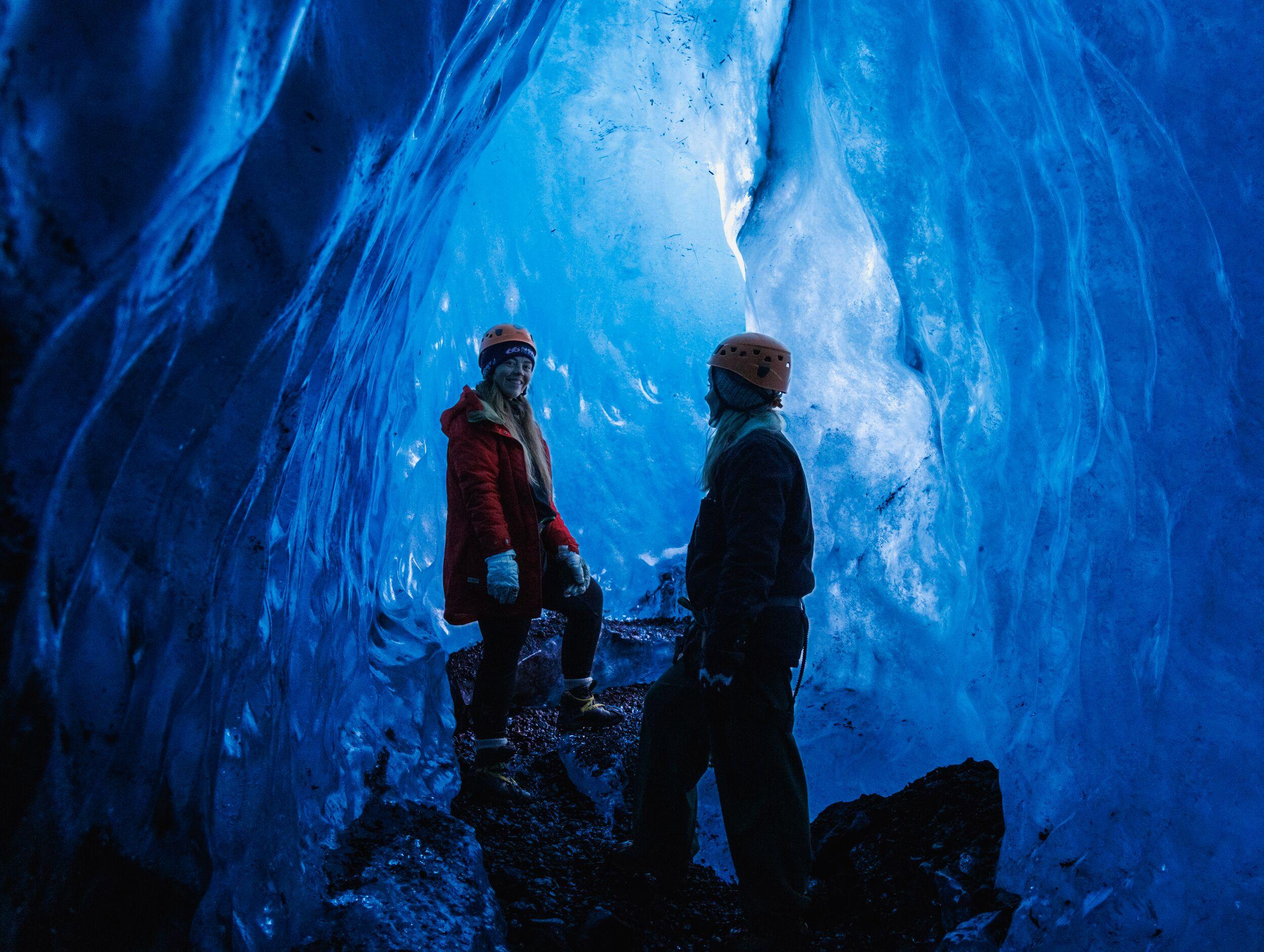 A person poses inside a glowing blue ice cave.