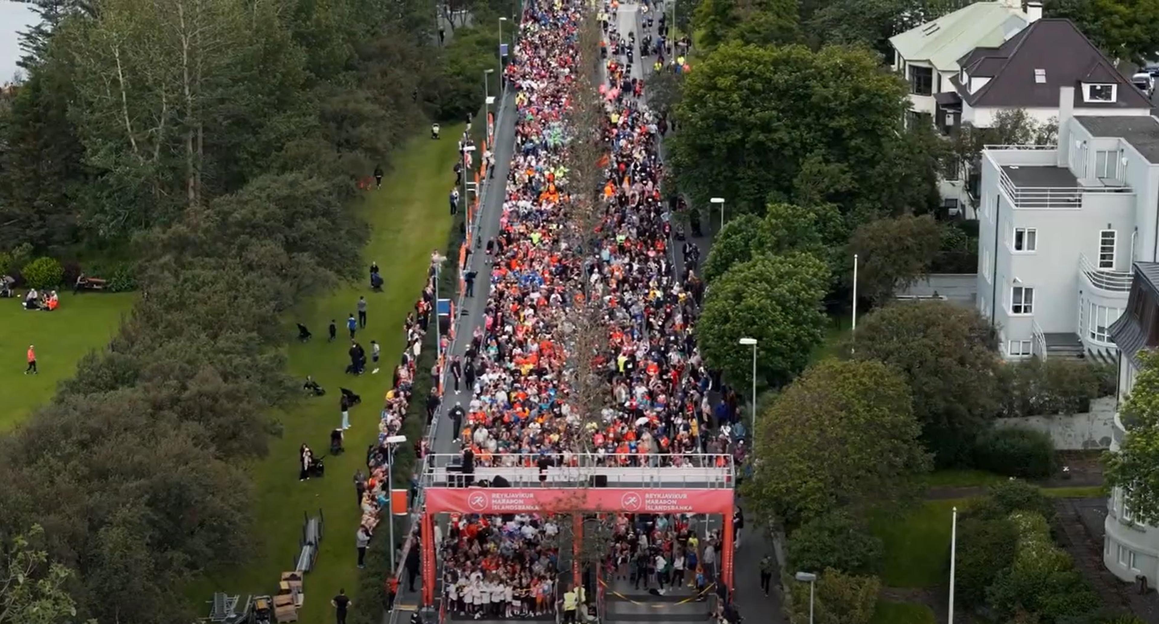 Aerial view of runners gathered at the starting line for the Reykjavík Marathon, with green trees and spectators lining the path.