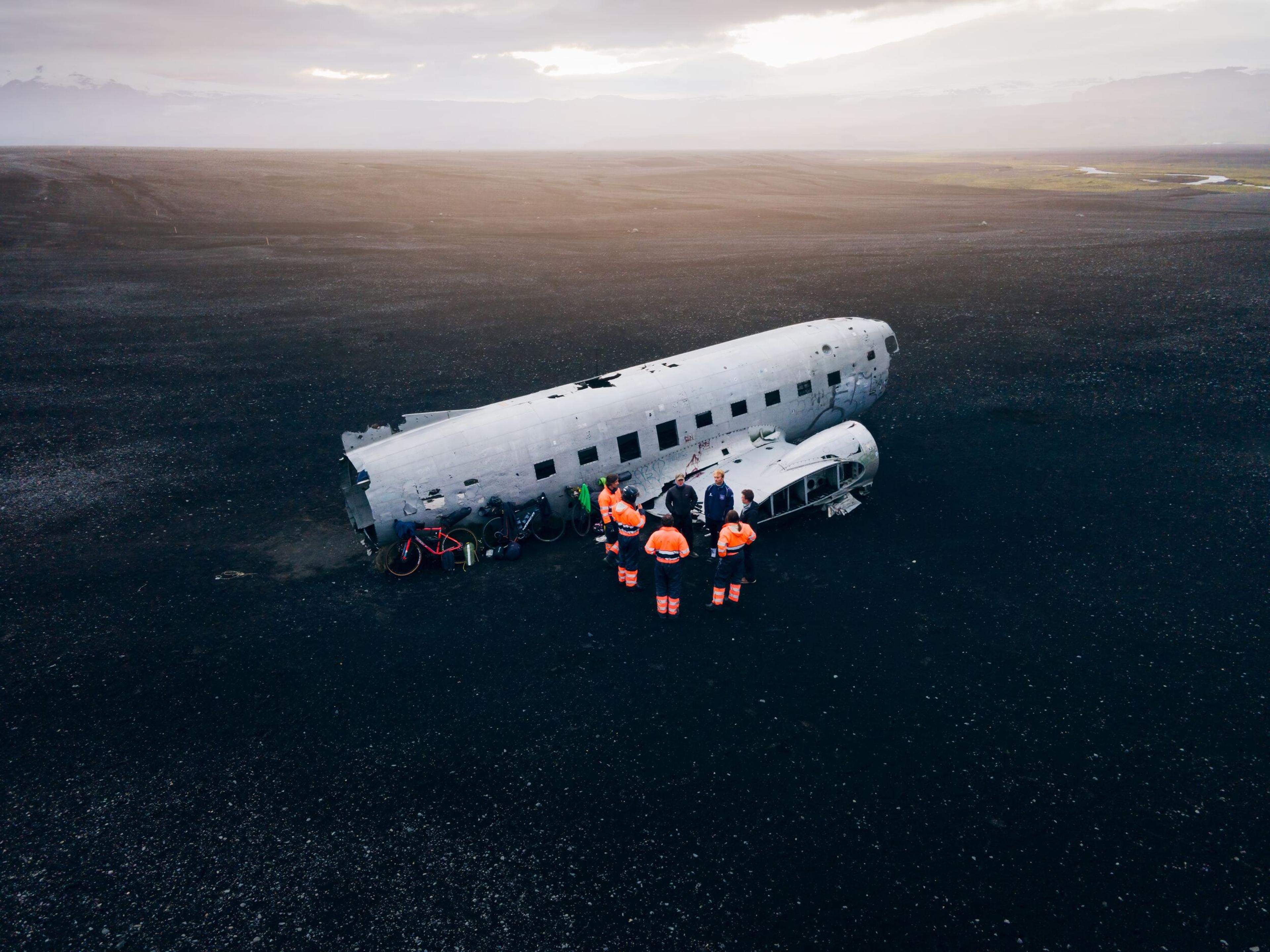 group of people around a dc3 plane wreck in the icelandic black sand beach