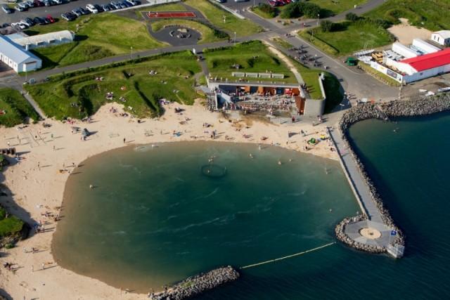 This image shows Nauthólsvík Geothermal Beach in Reykjavík, Iceland, a popular spot featuring golden sands and a sheltered lagoon. The beach combines natural beauty with warm geothermal waters, making it a unique and inviting location for locals and visitors alike.