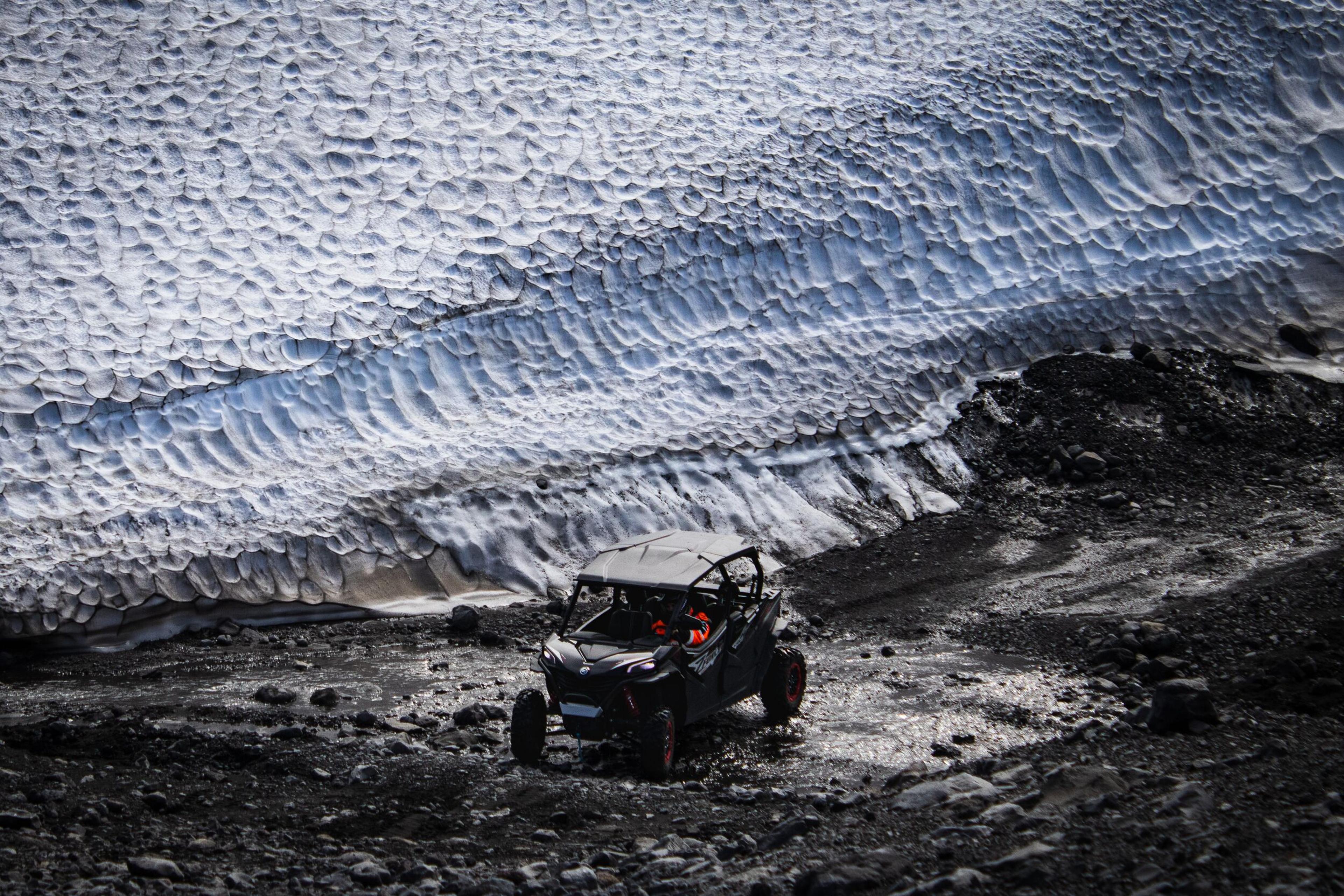 Off-road buggy driving on rocky terrain near a snow-covered slope on the South Coast of Iceland.