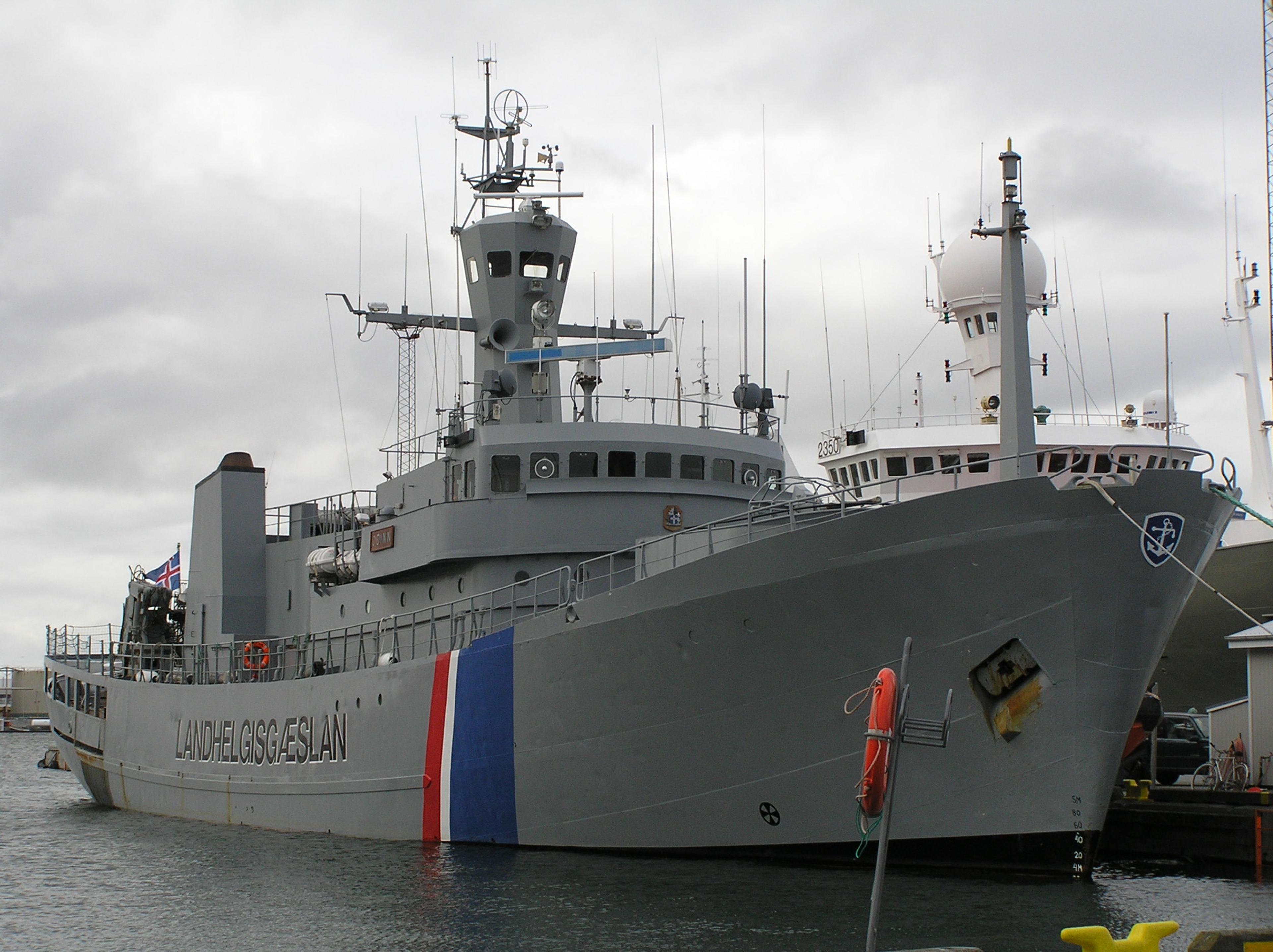 Icelandic Coast Guard ship docked at a harbor under a gray, cloudy sky.