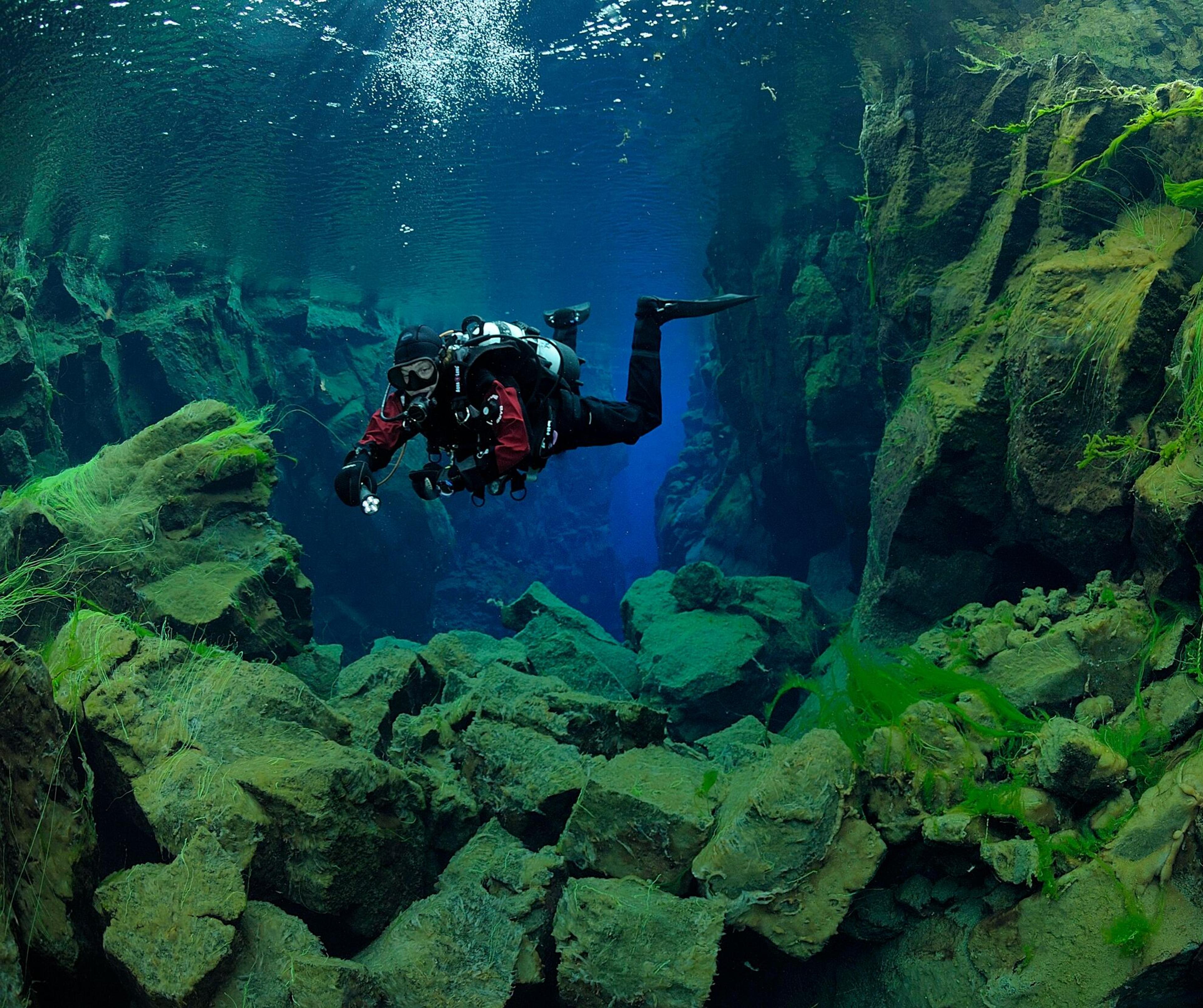 Diver descending into the crystal-clear depths of Silfra fissure, situated between tectonic plates.