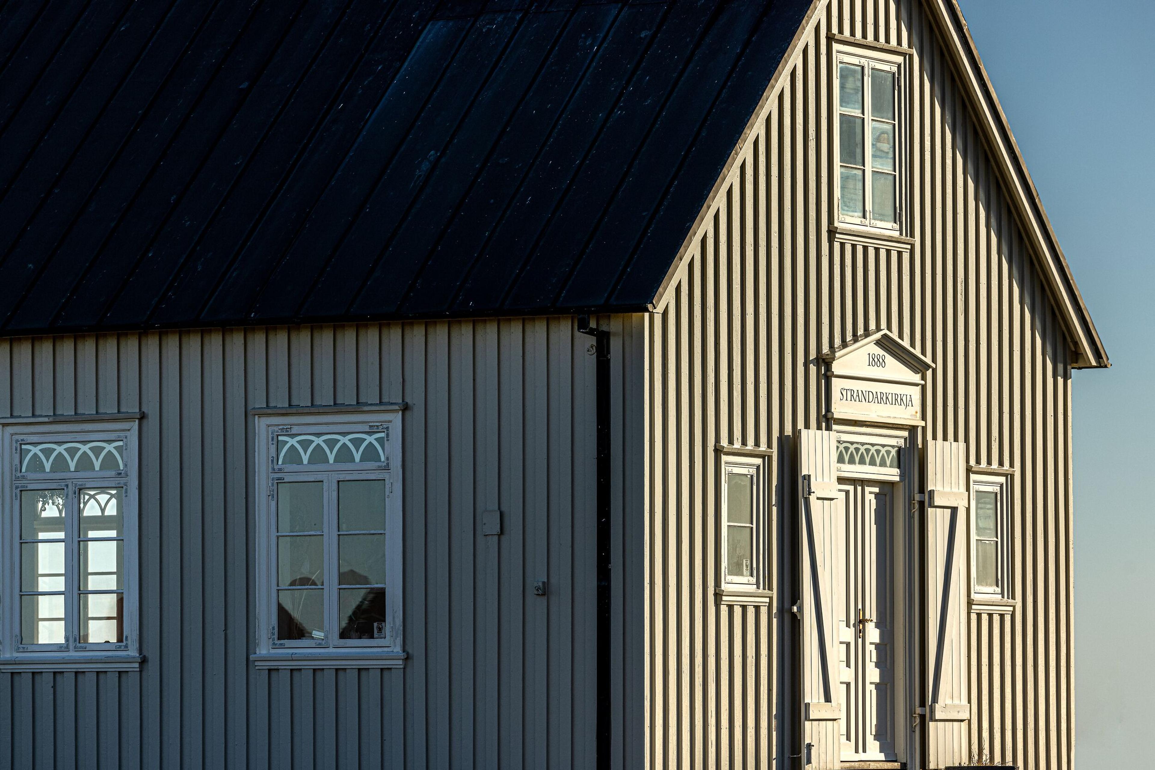 Exterior of a traditional Icelandic church featuring a black roof, white-framed windows, and intricate trim, highlighting classic Nordic architecture.