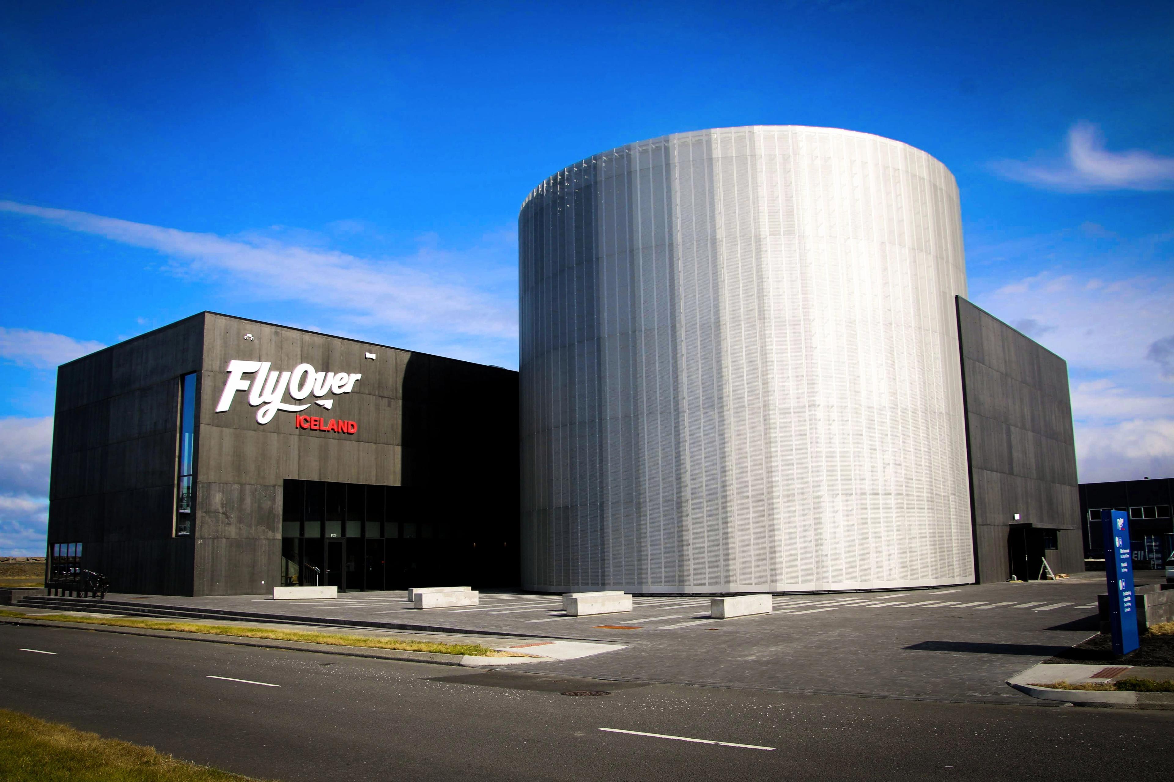 The modern FlyOver Iceland building with a dark rectangular section and a large, light gray cylindrical section.