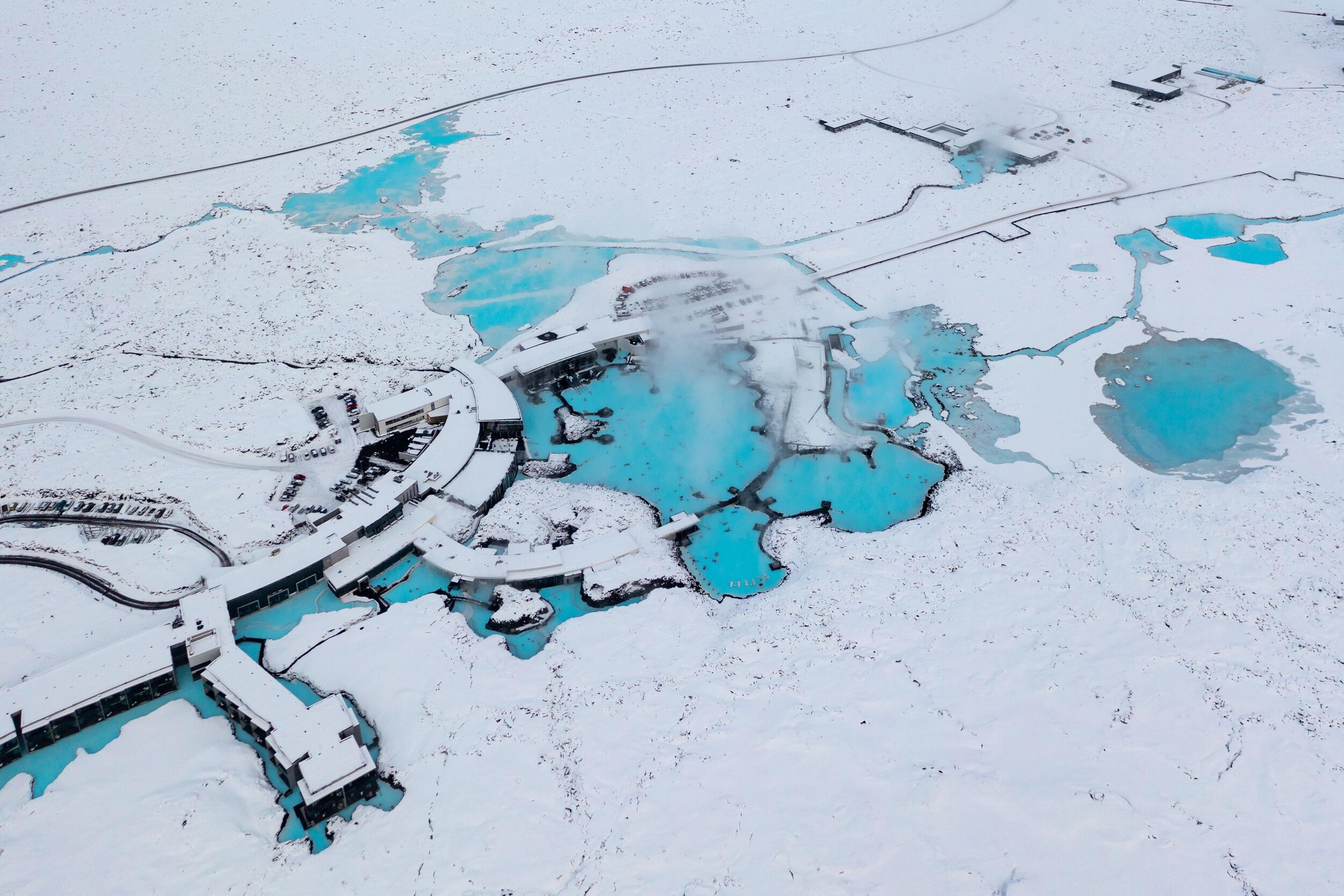 Aerial view of the Blue Lagoon geothermal spa in Iceland, with vivid turquoise water, steam, and snow-covered buildings.