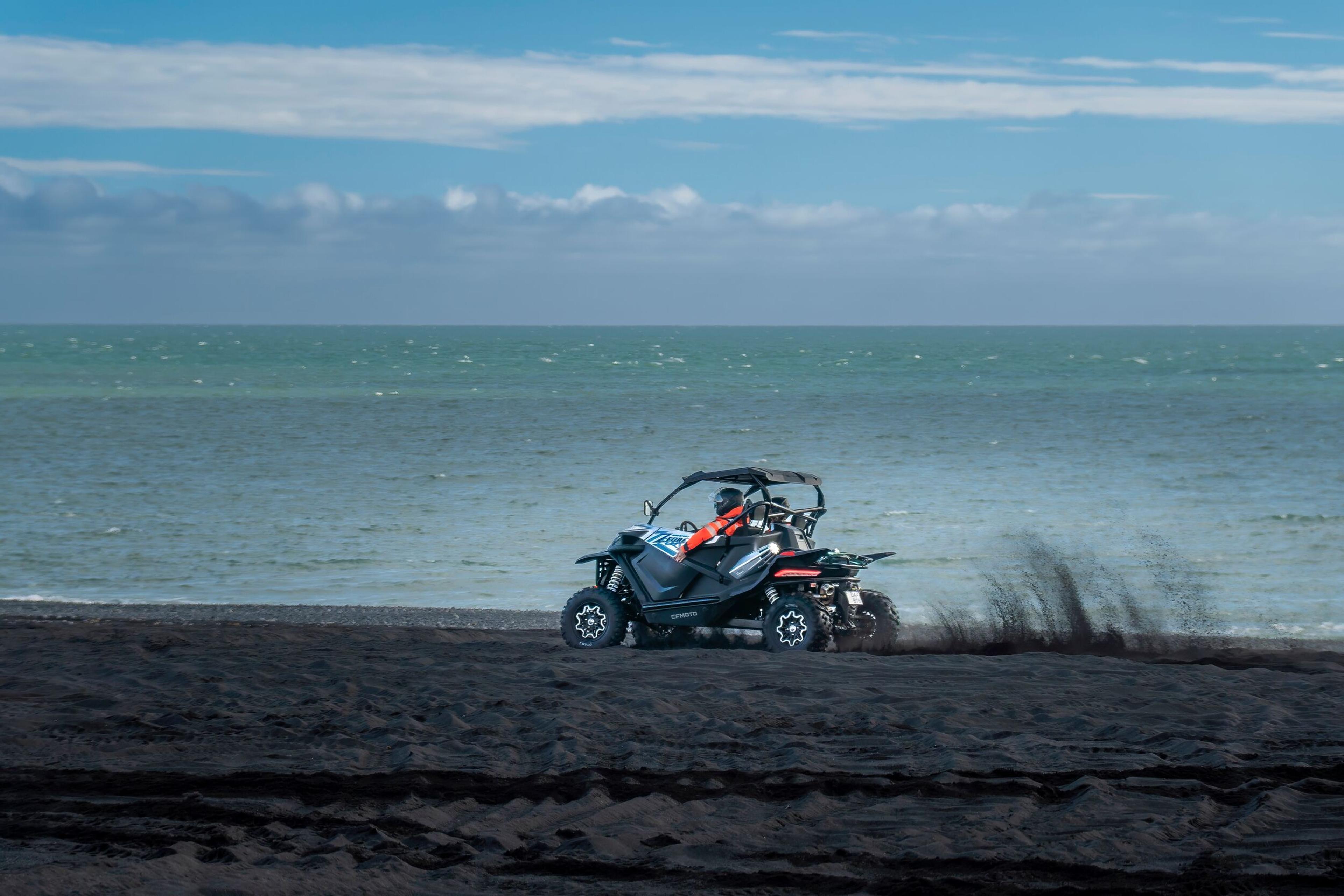 A buggy parked on a black sand beach with the blue ocean in the background under a partly cloudy sky, indicative of a buggy tour in Iceland.