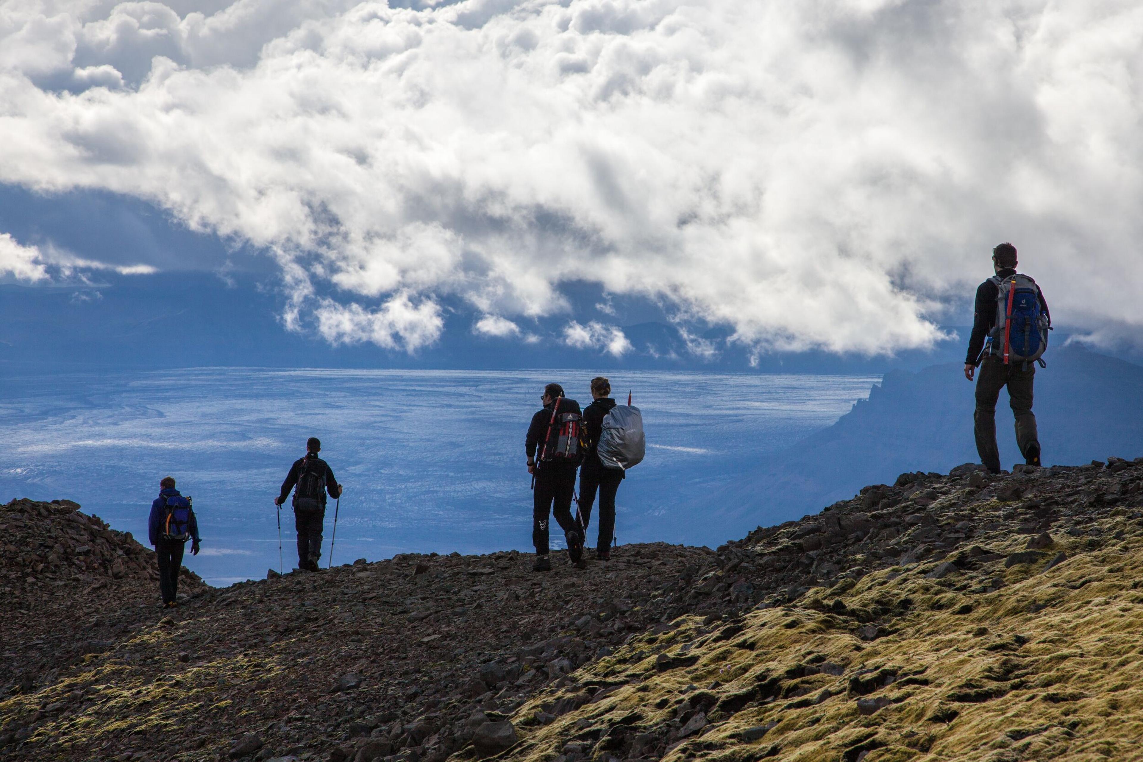 Five hikers on a rocky, mossy slope overlooking a vast cloudy landscape.