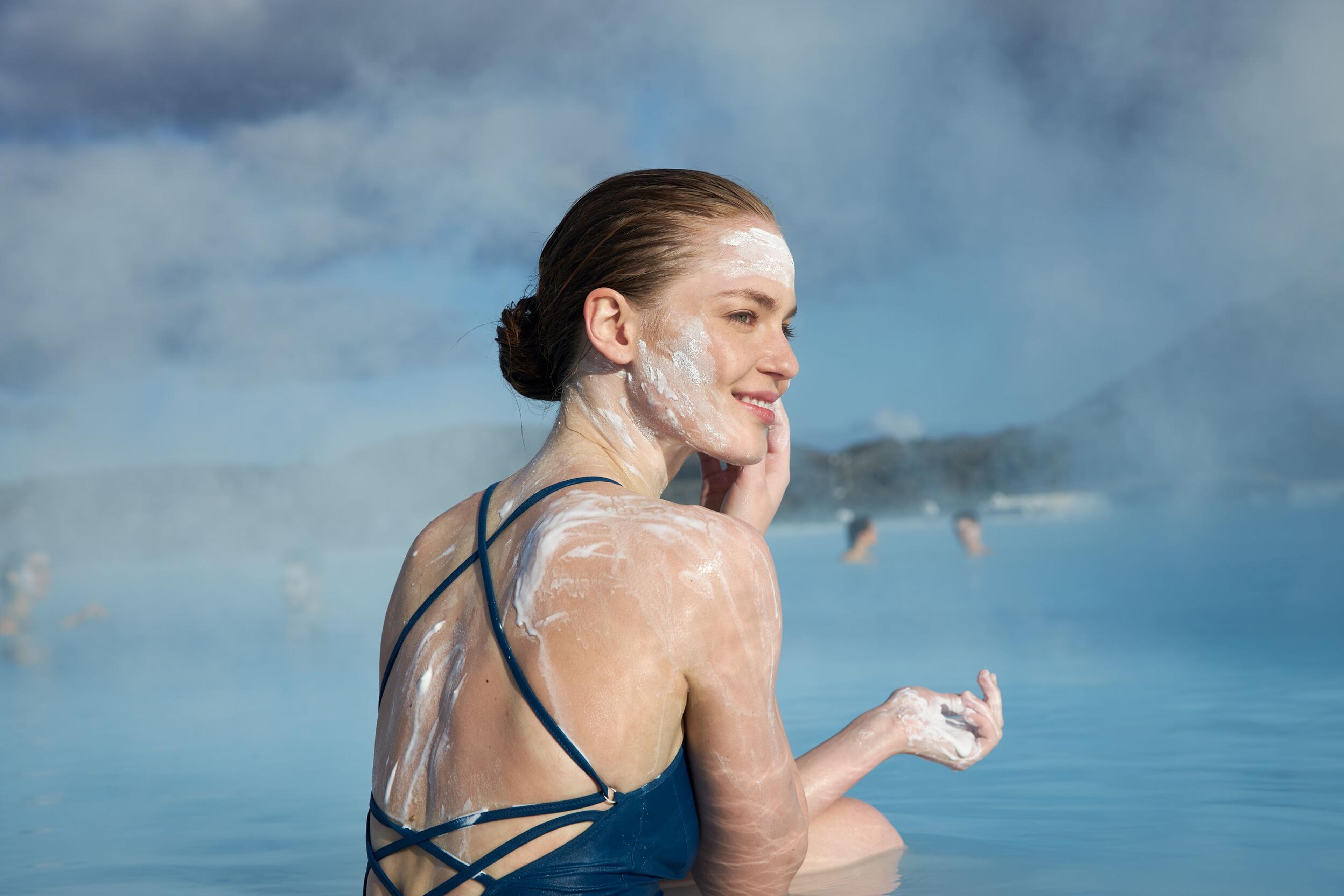 A woman using silica mud treatment by the water at Blue Lagoon, Iceland.