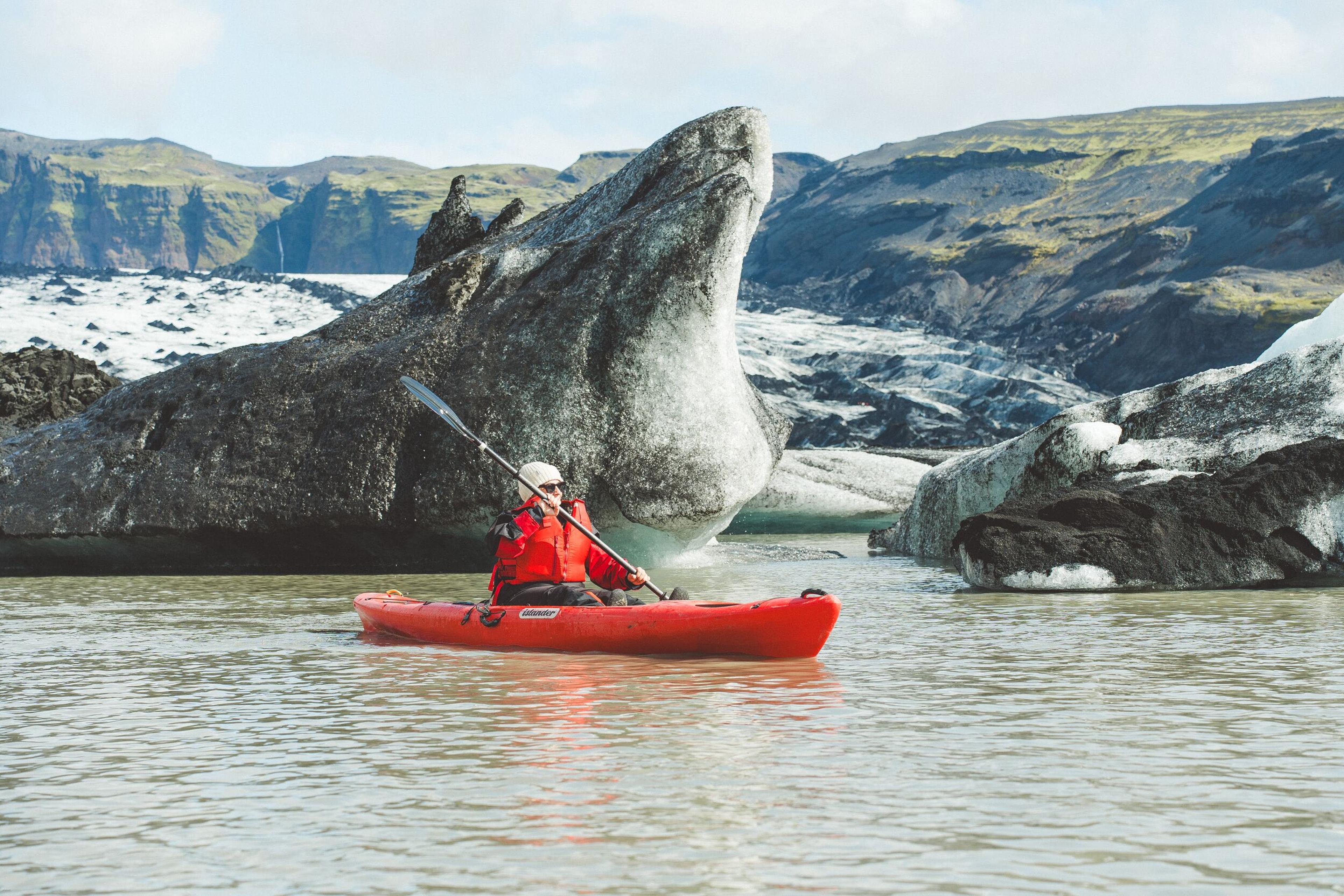 Person in a red kayak on a glacial lake with icebergs and mountains.