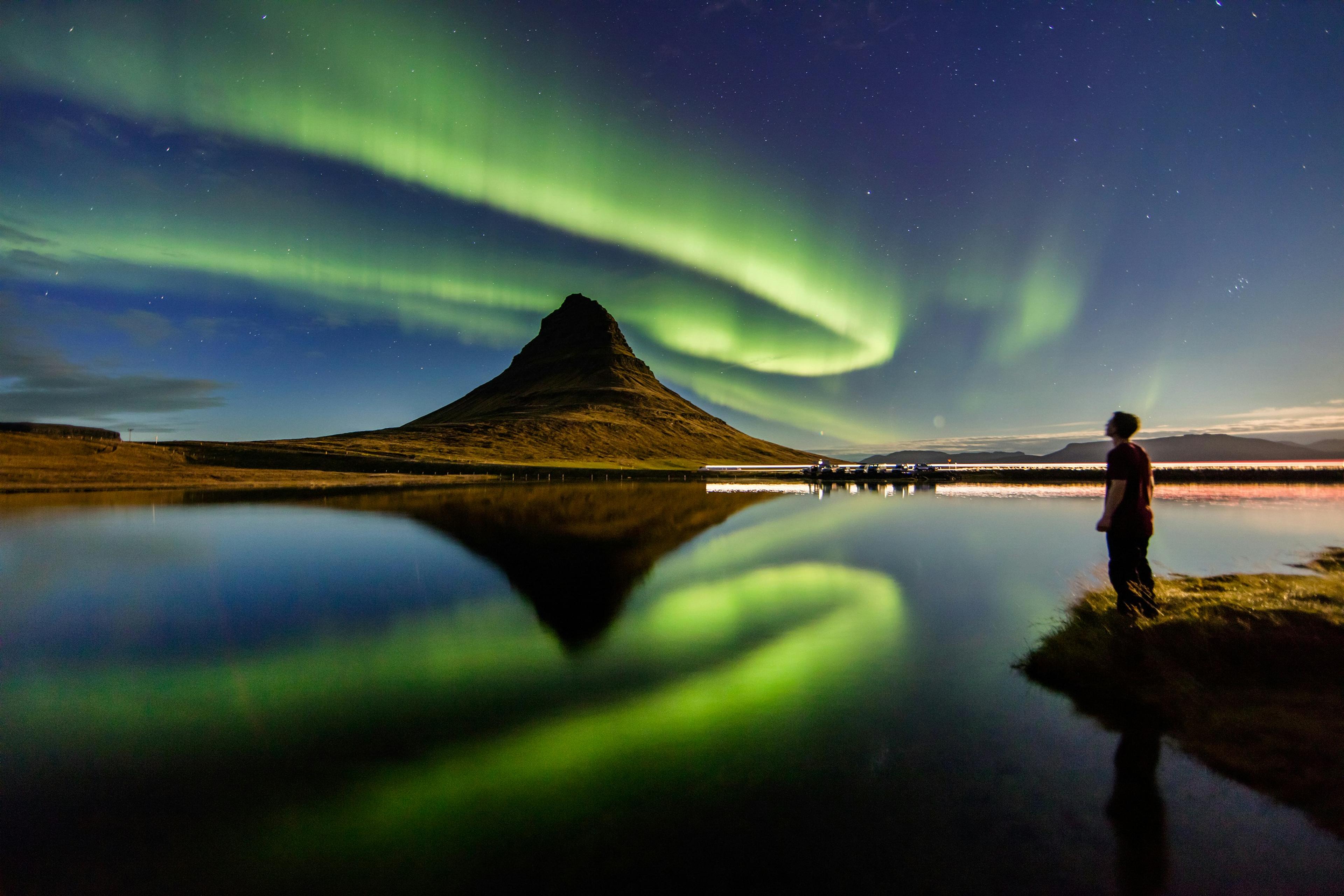 A person looking at the Northern Lights that illuminates the sky above Kirkjufekk mountain in West Iceland