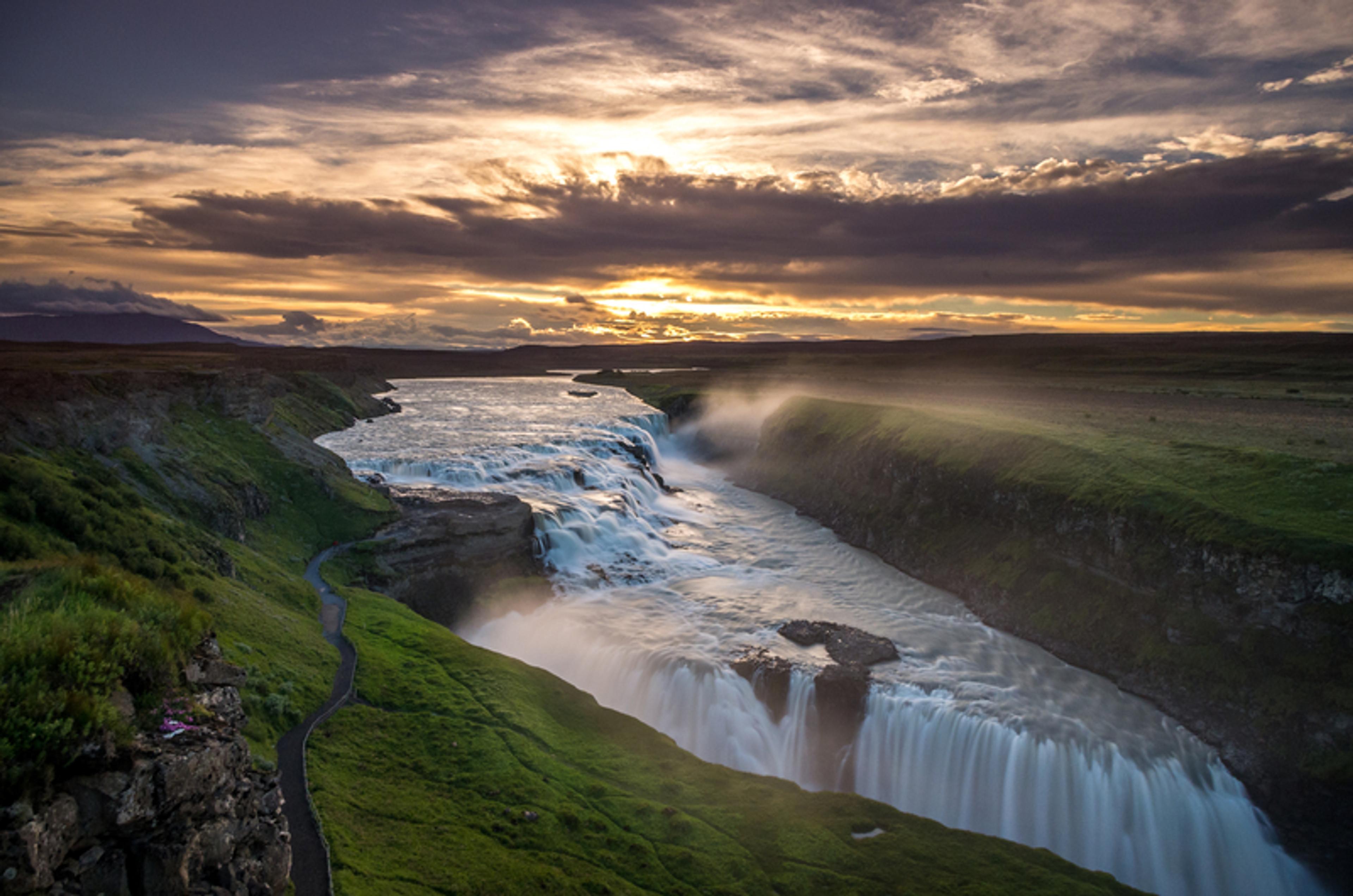 there is a waterfall in the middle of a river at sunset .
