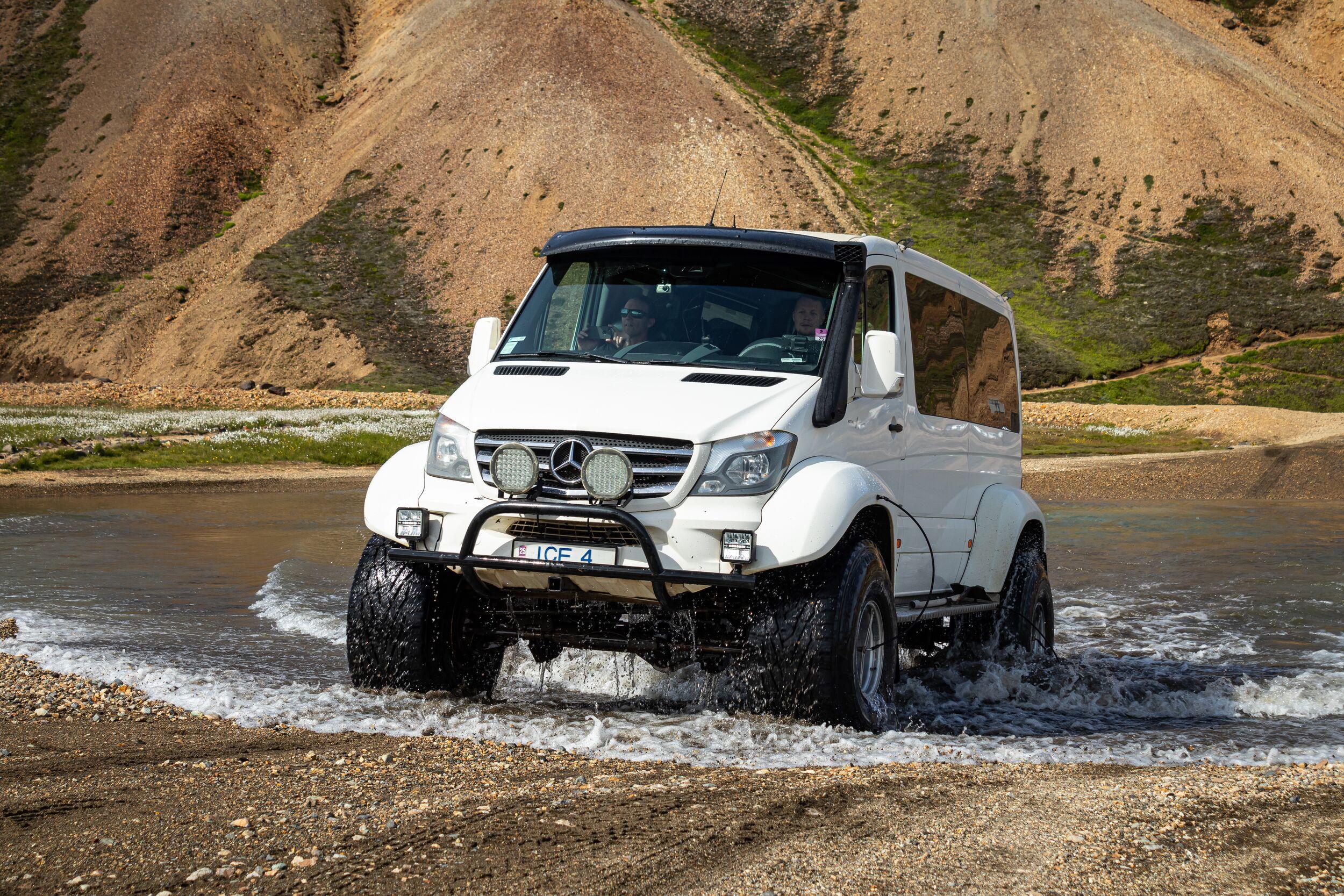 a white mercedes benz sprinter is driving through a river .
