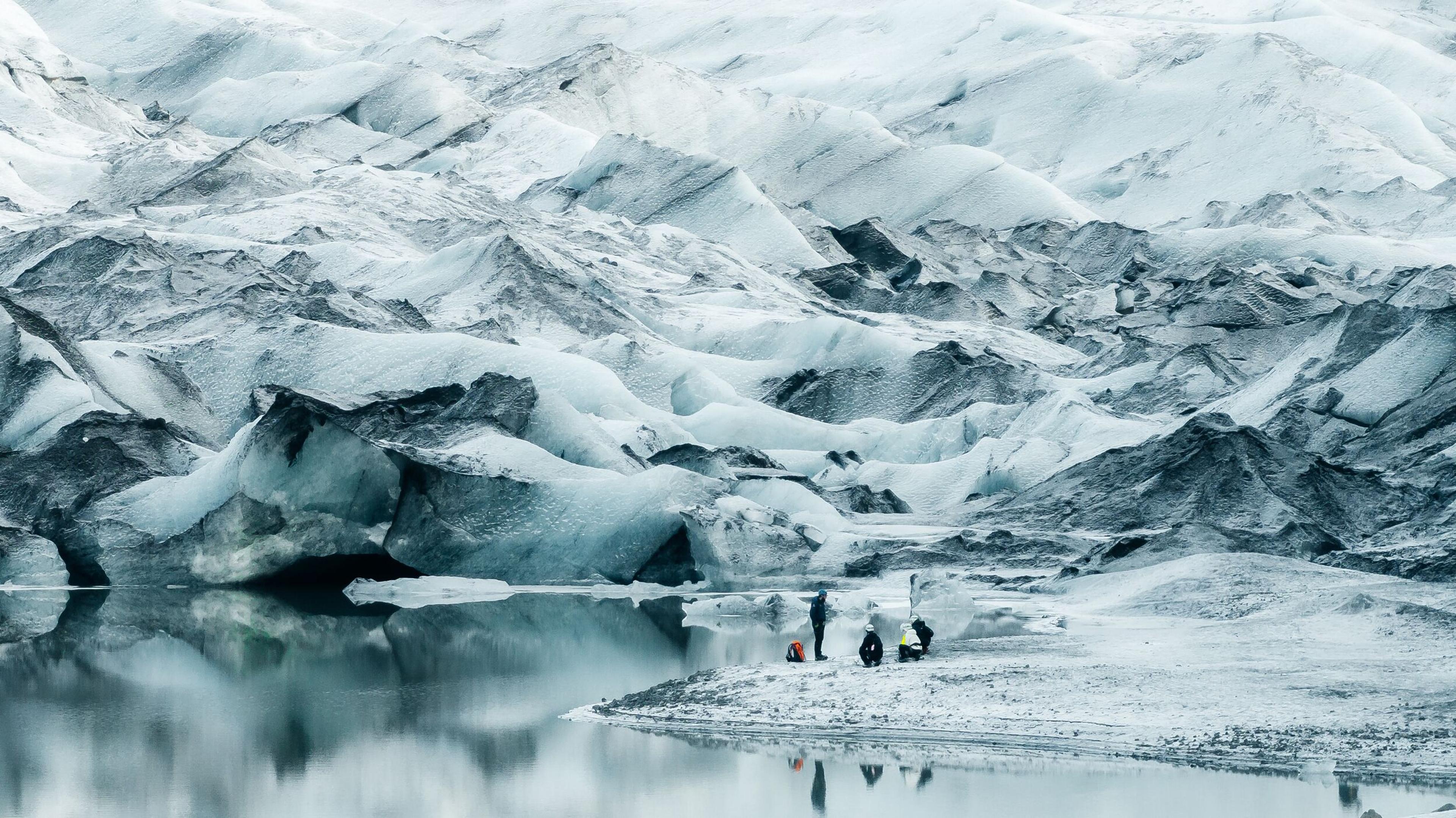People standing by a glacial lake with a vast glacier behind them.