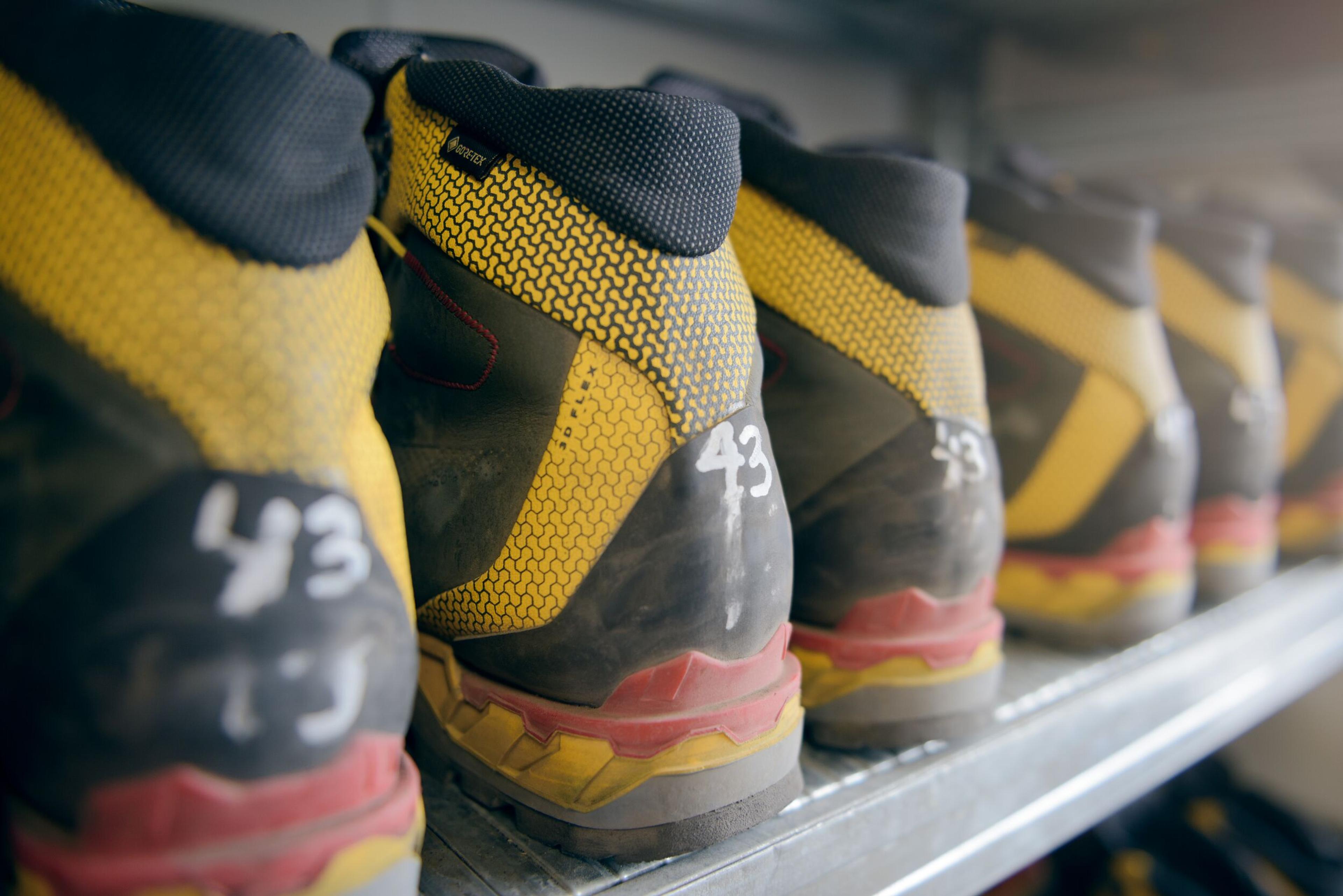  A row of yellow and black hiking boots labeled with size 43, neatly arranged on a shelf.