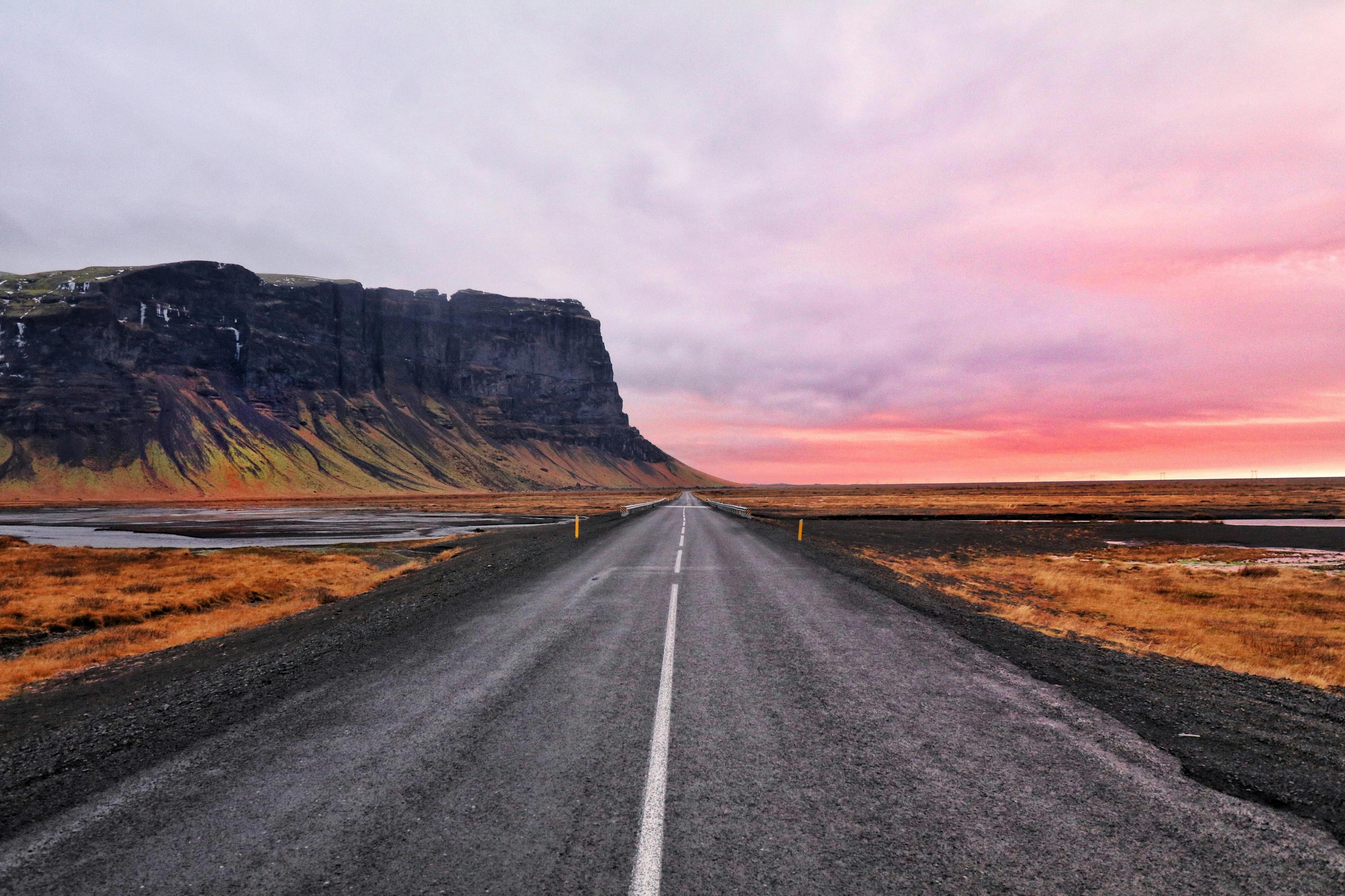 an empty road with a mountain in the background at sunset .