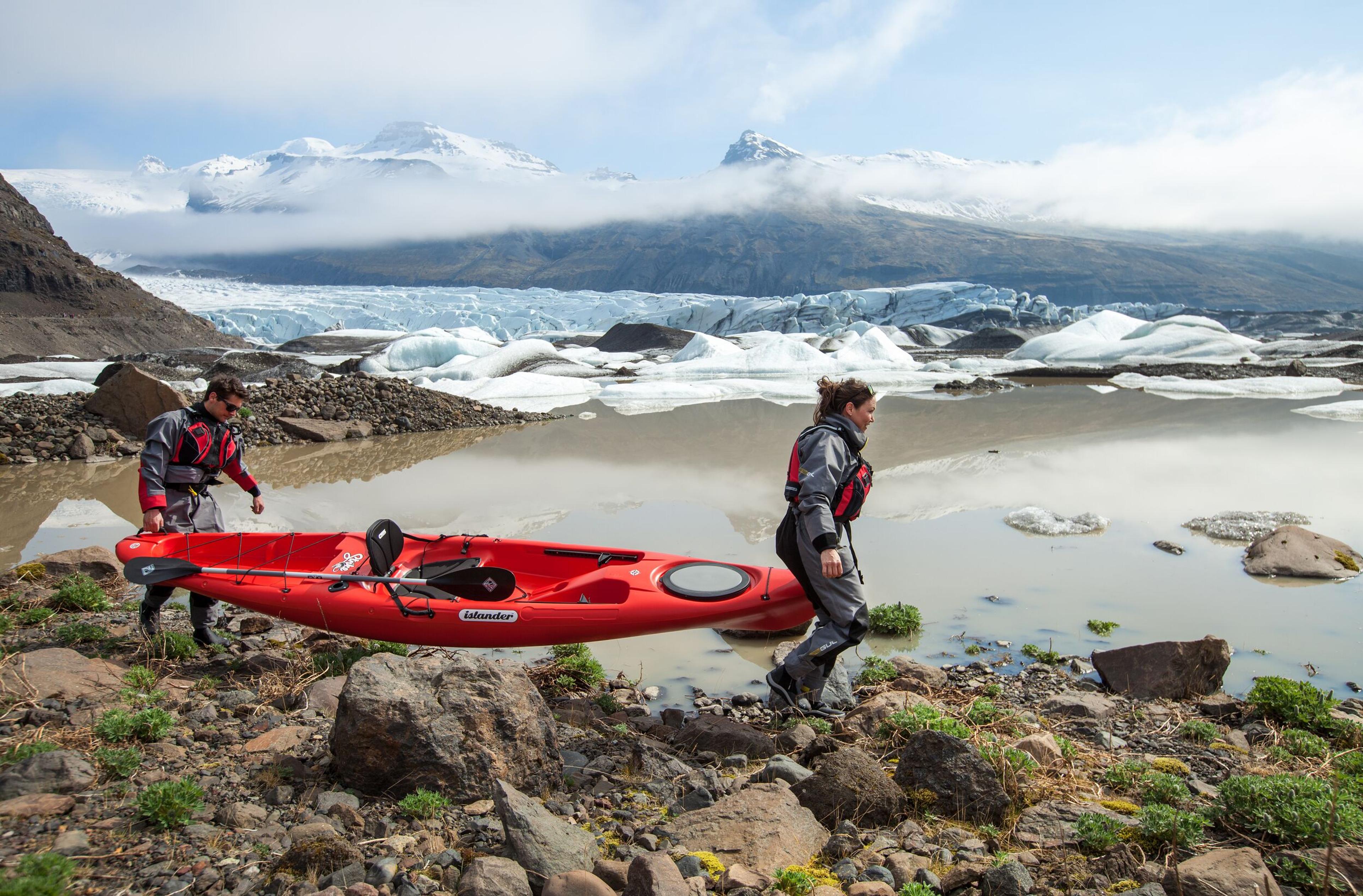 Two people carrying a kayak near a glacier lagoon