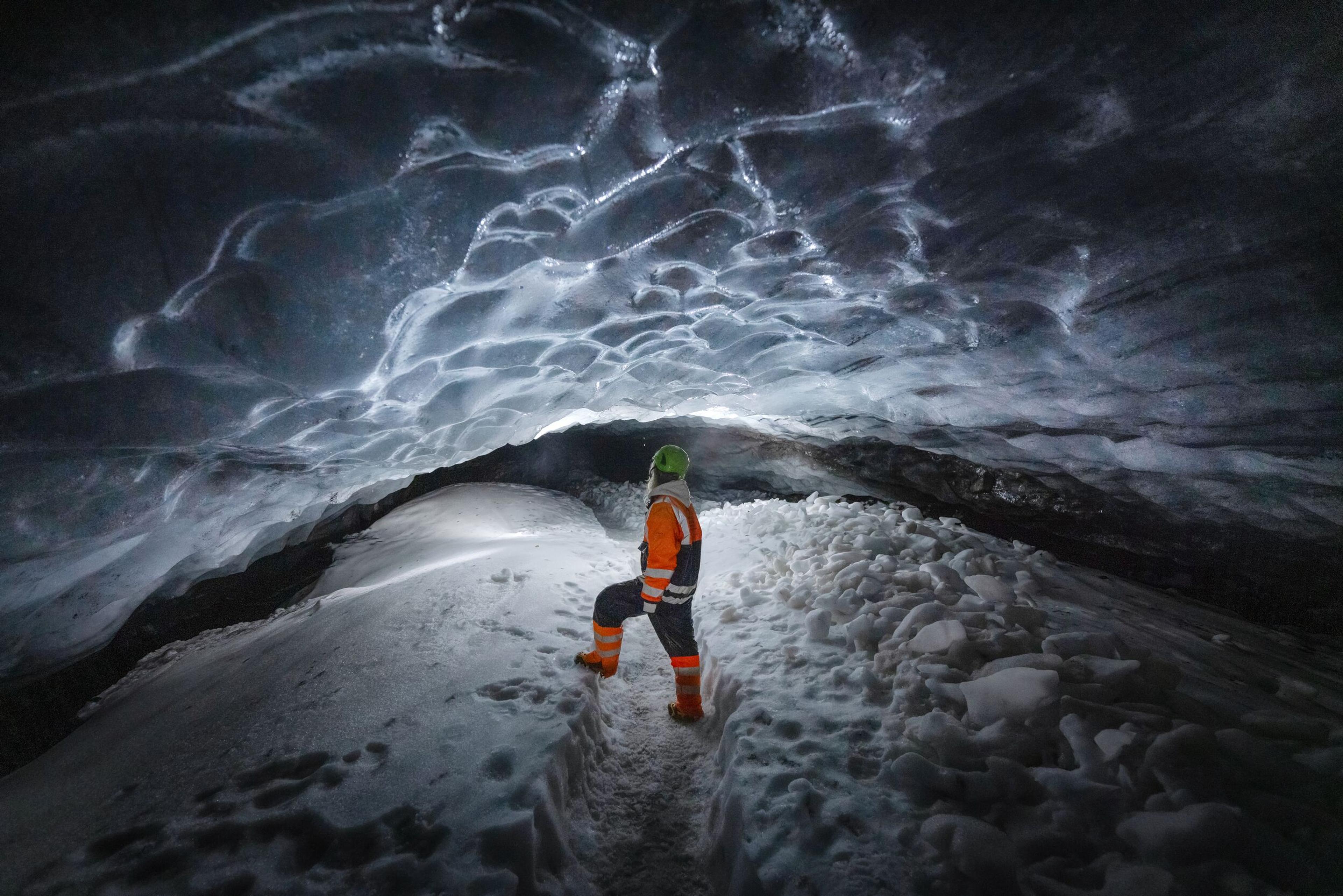 A tourist exploring a blue ice cave with intricate ceiling patterns.