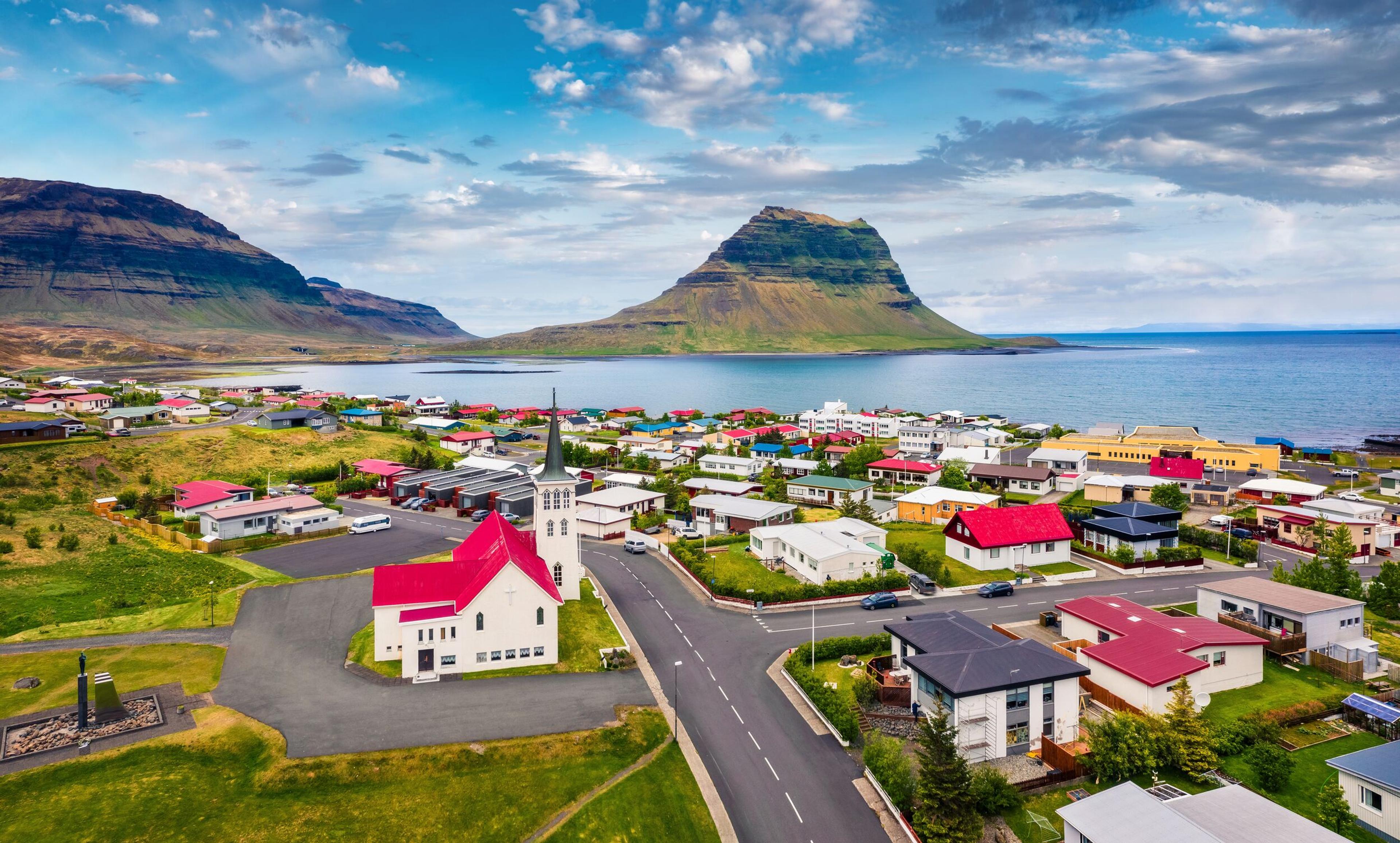 A quaint colorful village on a sunlit summer day, with the iconic Kirkjufell mountain and the shimmering sea framing the backdrop.