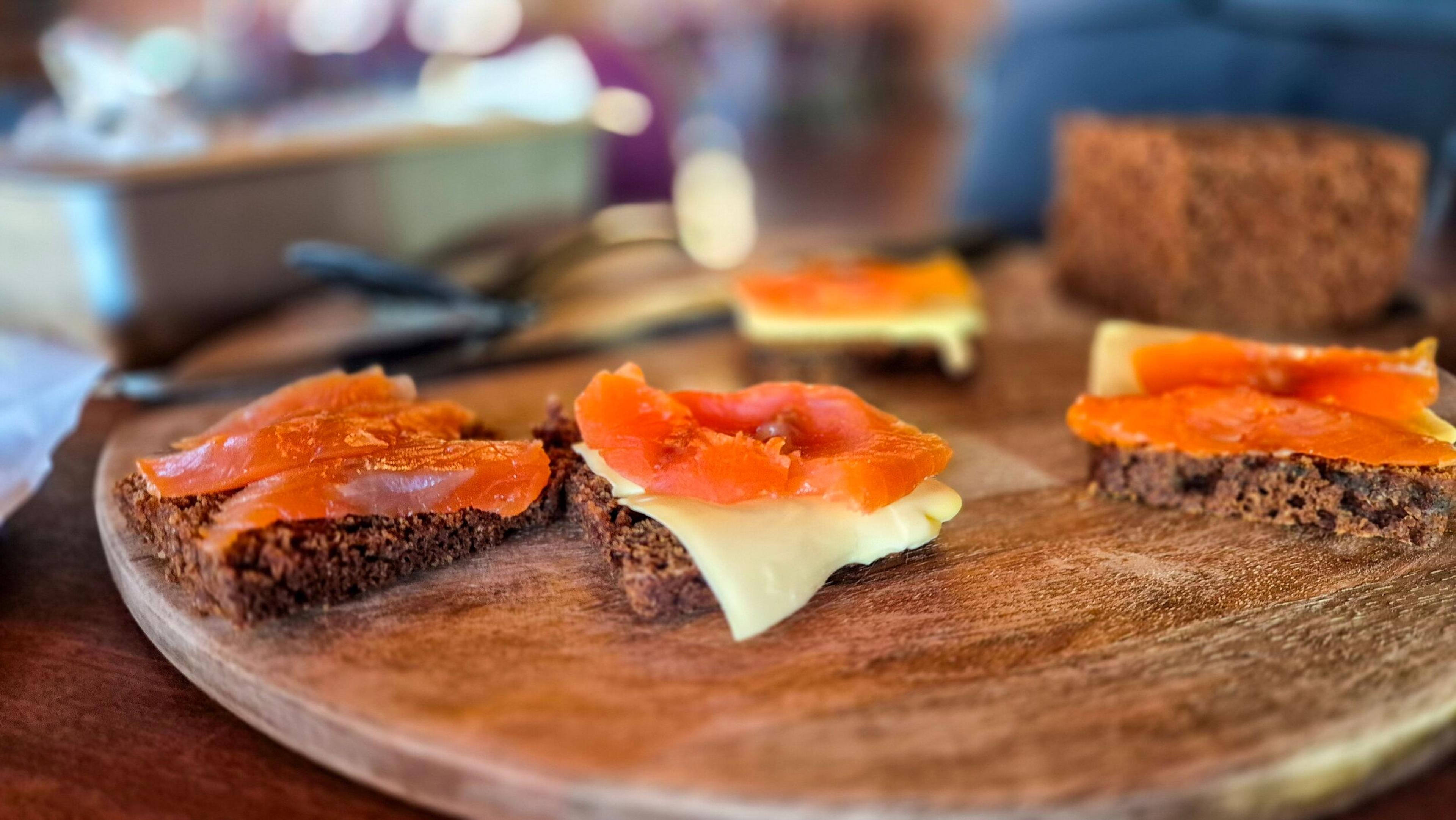 Open-faced sandwiches with dark bread, cheese, and salmon on a wooden board.