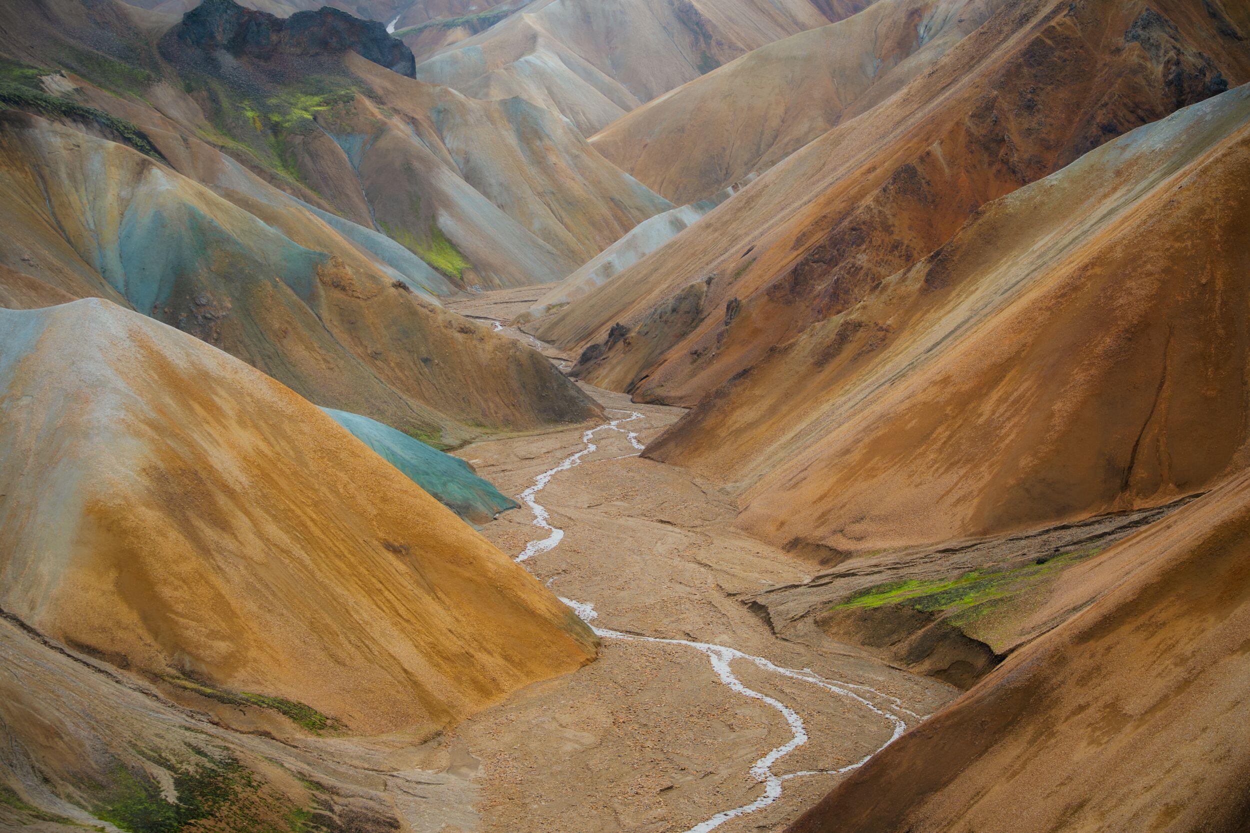 A winding riverbed through a valley of colorful, undulating mountains.