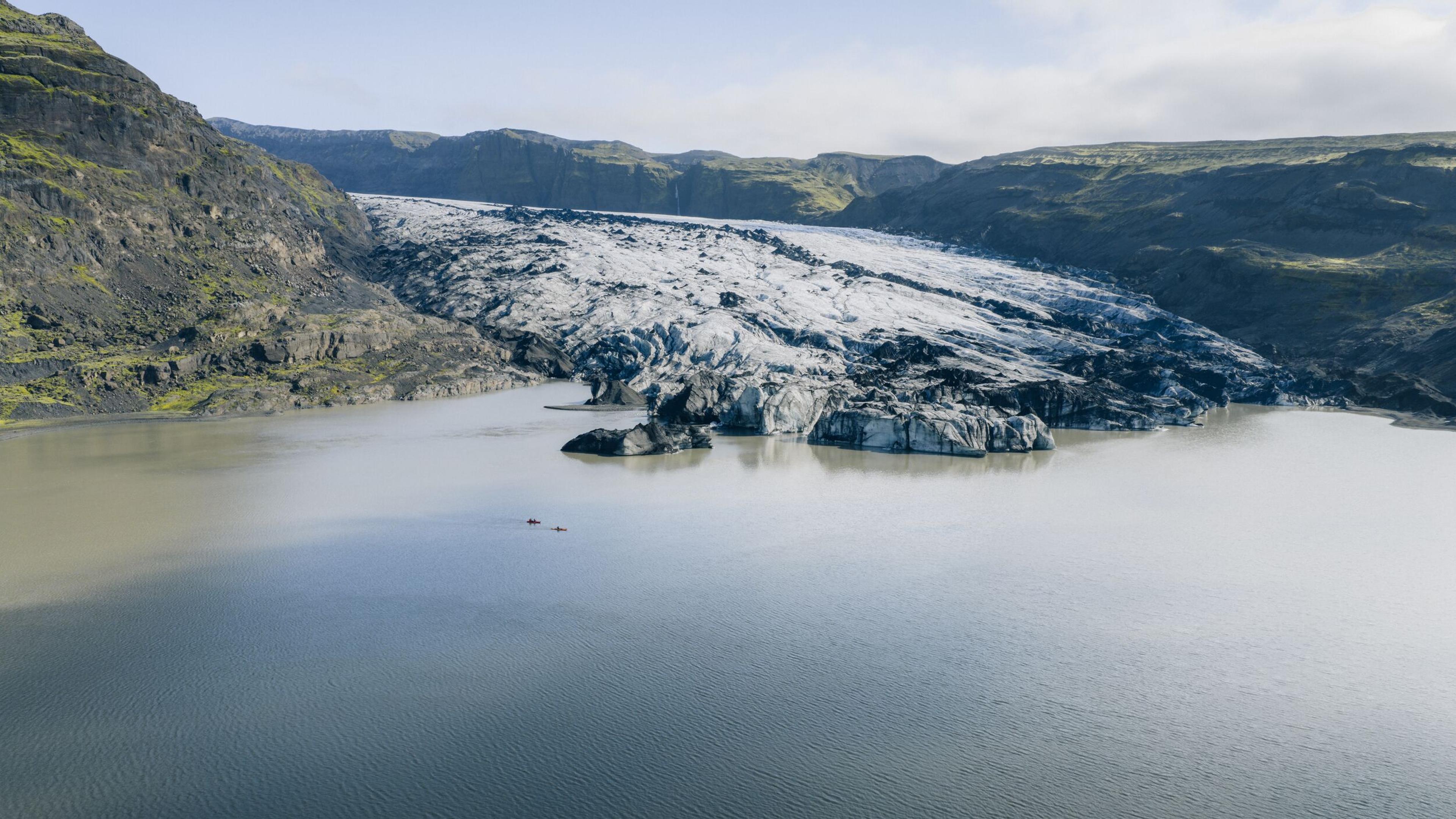 A glacier meets a lake surrounded by dark mountains, with two small red kayaks.