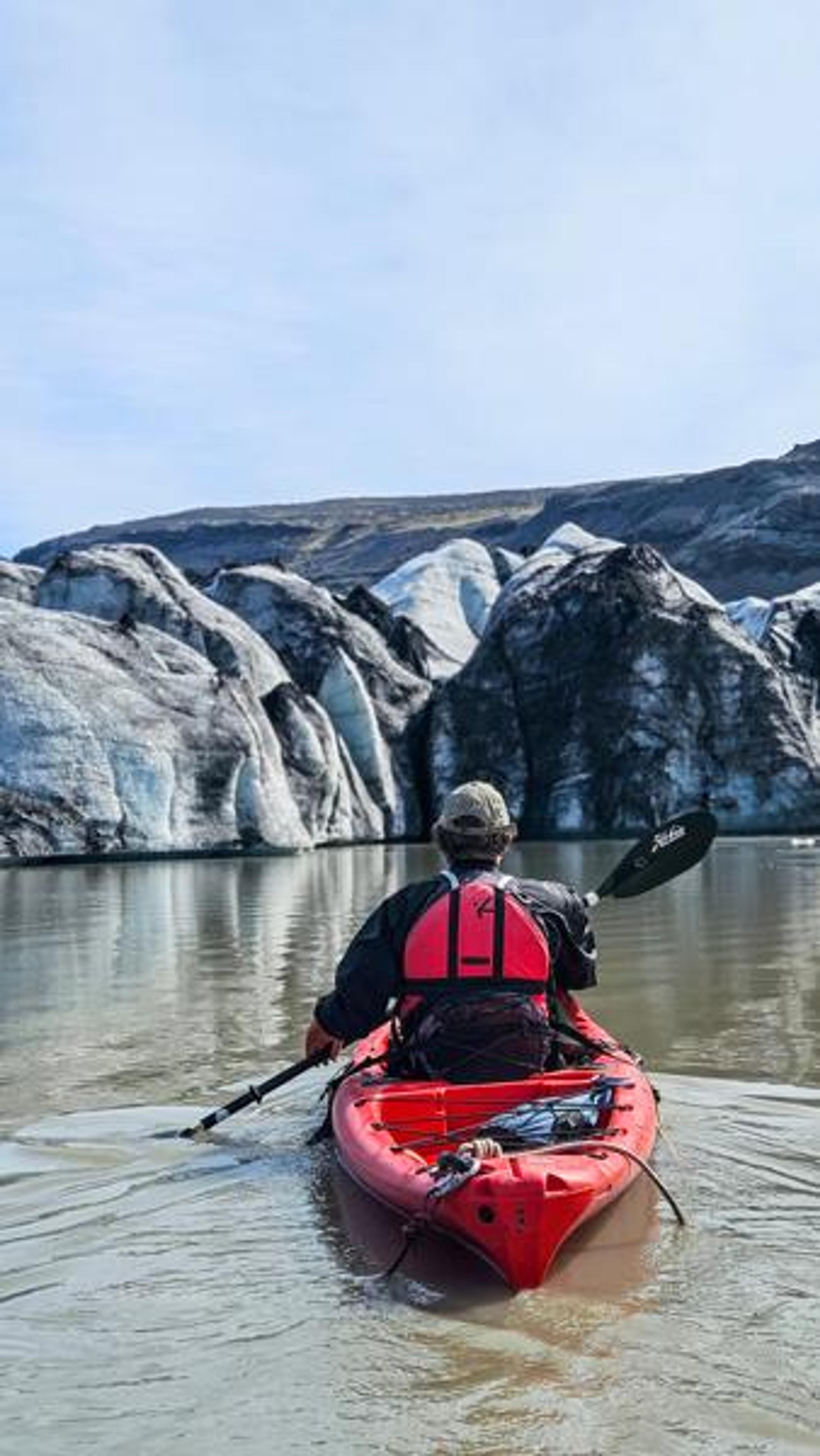 Person in a red kayak paddling towards large grey and white glacial ice formations.