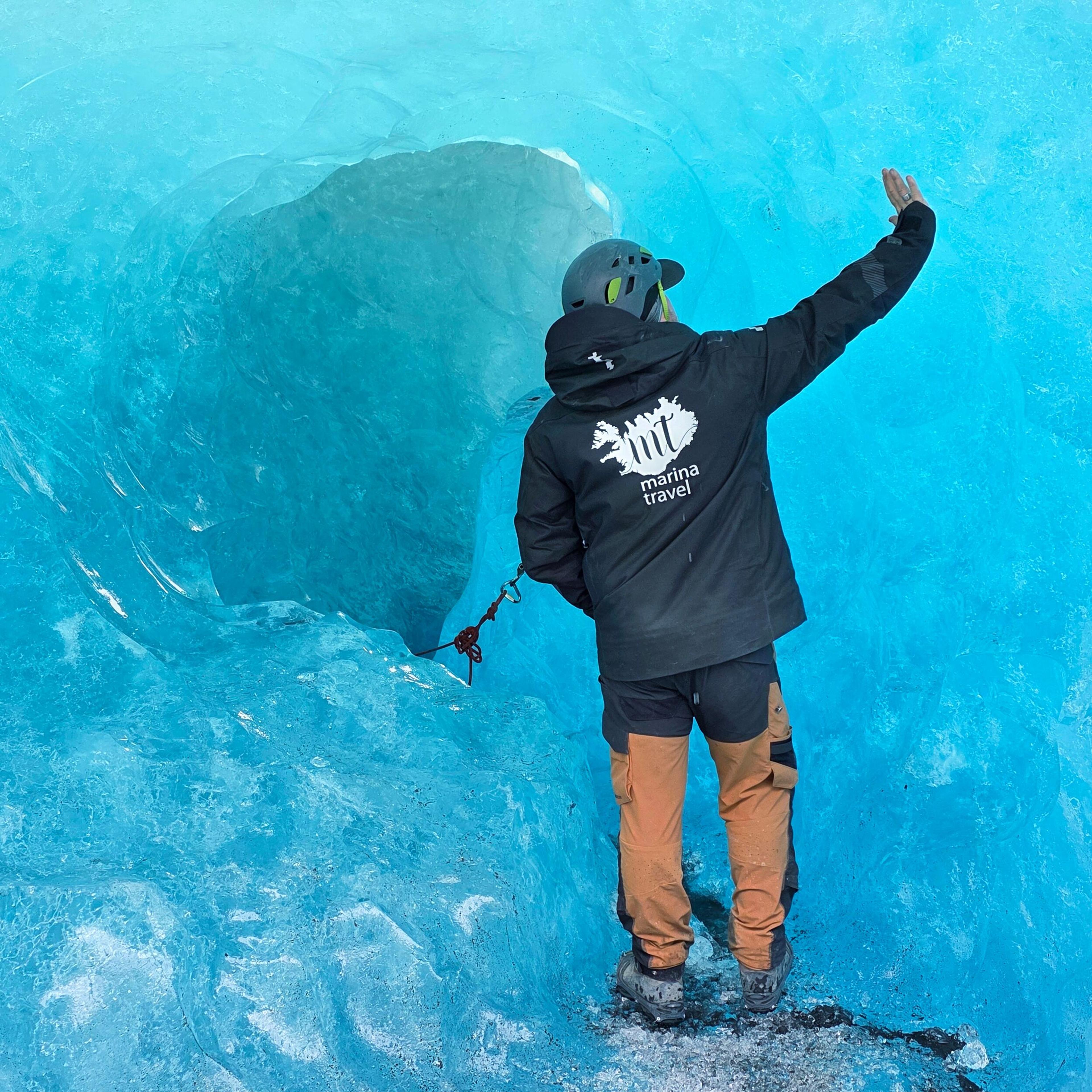 A person in a helmet and jacket inside a vivid blue ice cave, hand touching the ice wall.