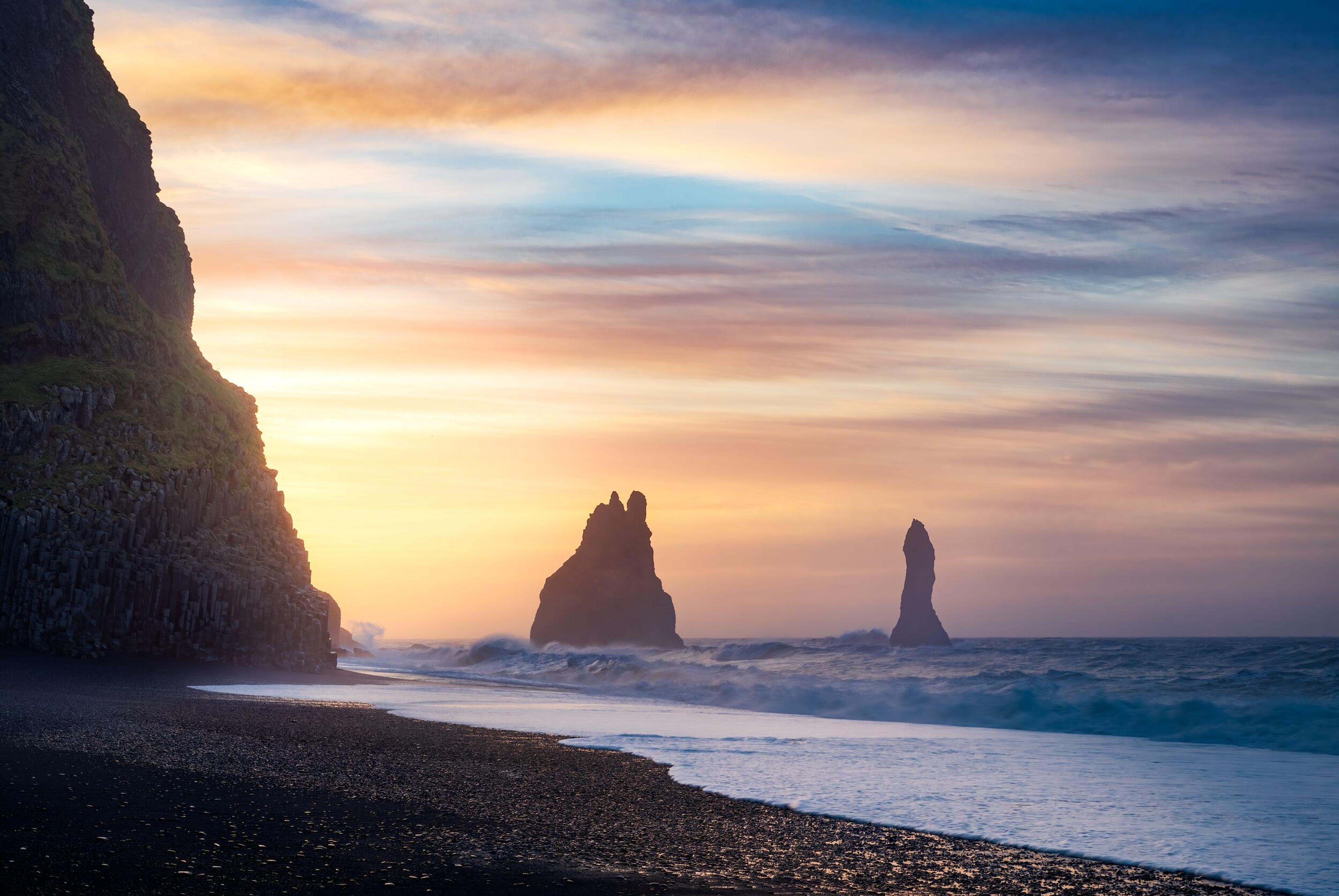 Black sand beach with basalt cliffs and sea stacks at sunrise or sunset.