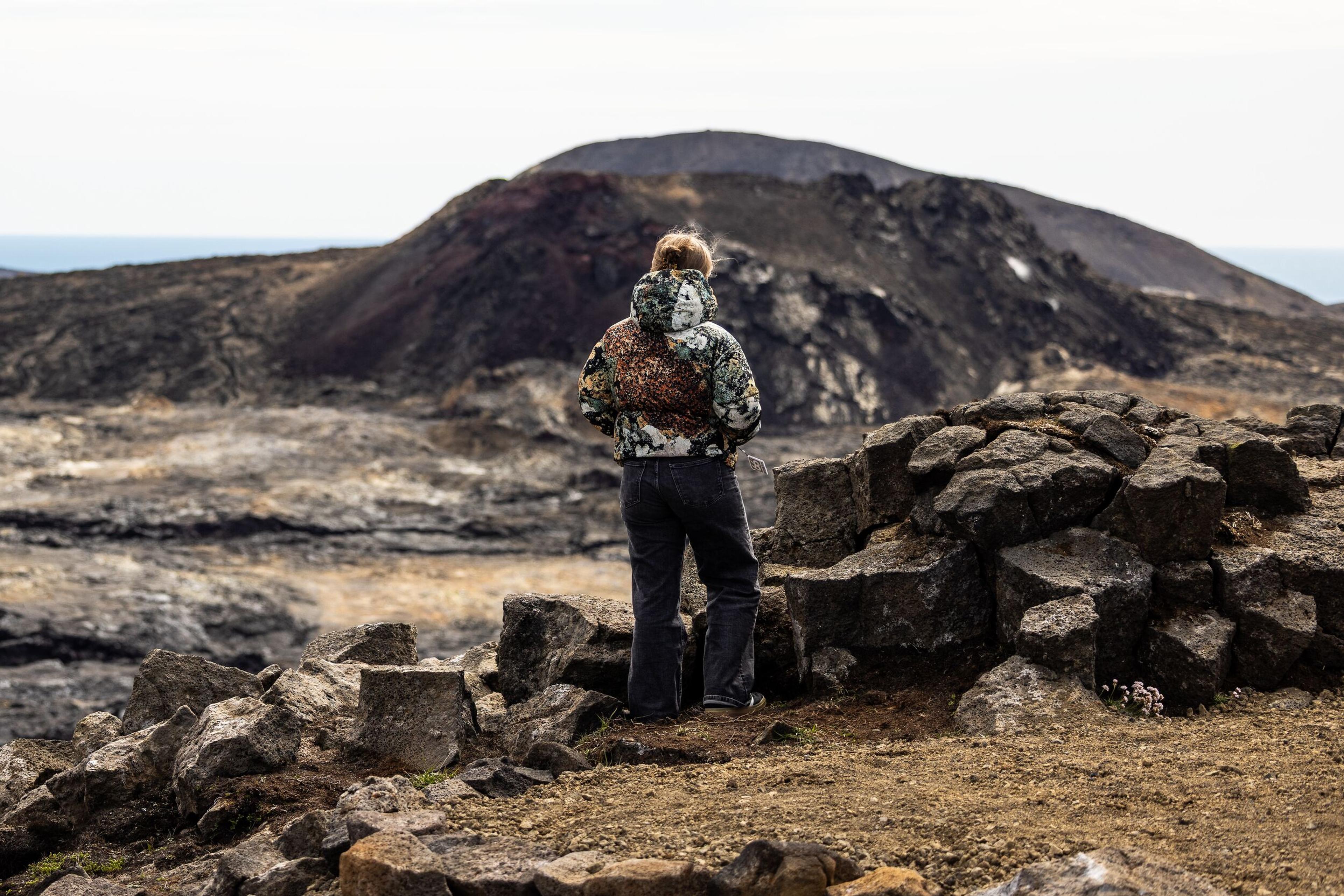 a woman is standing on top of a rocky hill looking at a mountain .