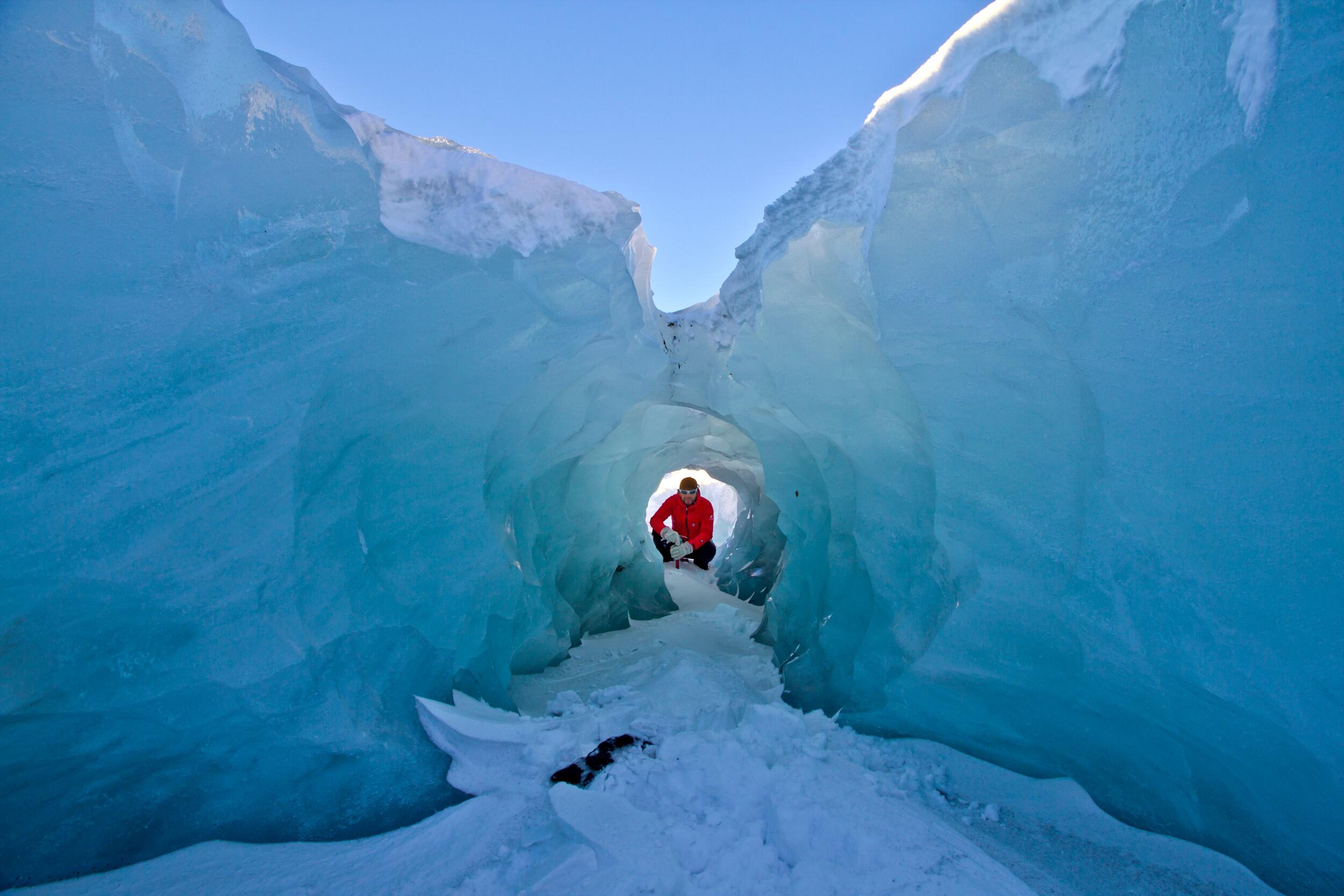 A person squatting to pose with a picturesque whole in the blue ice