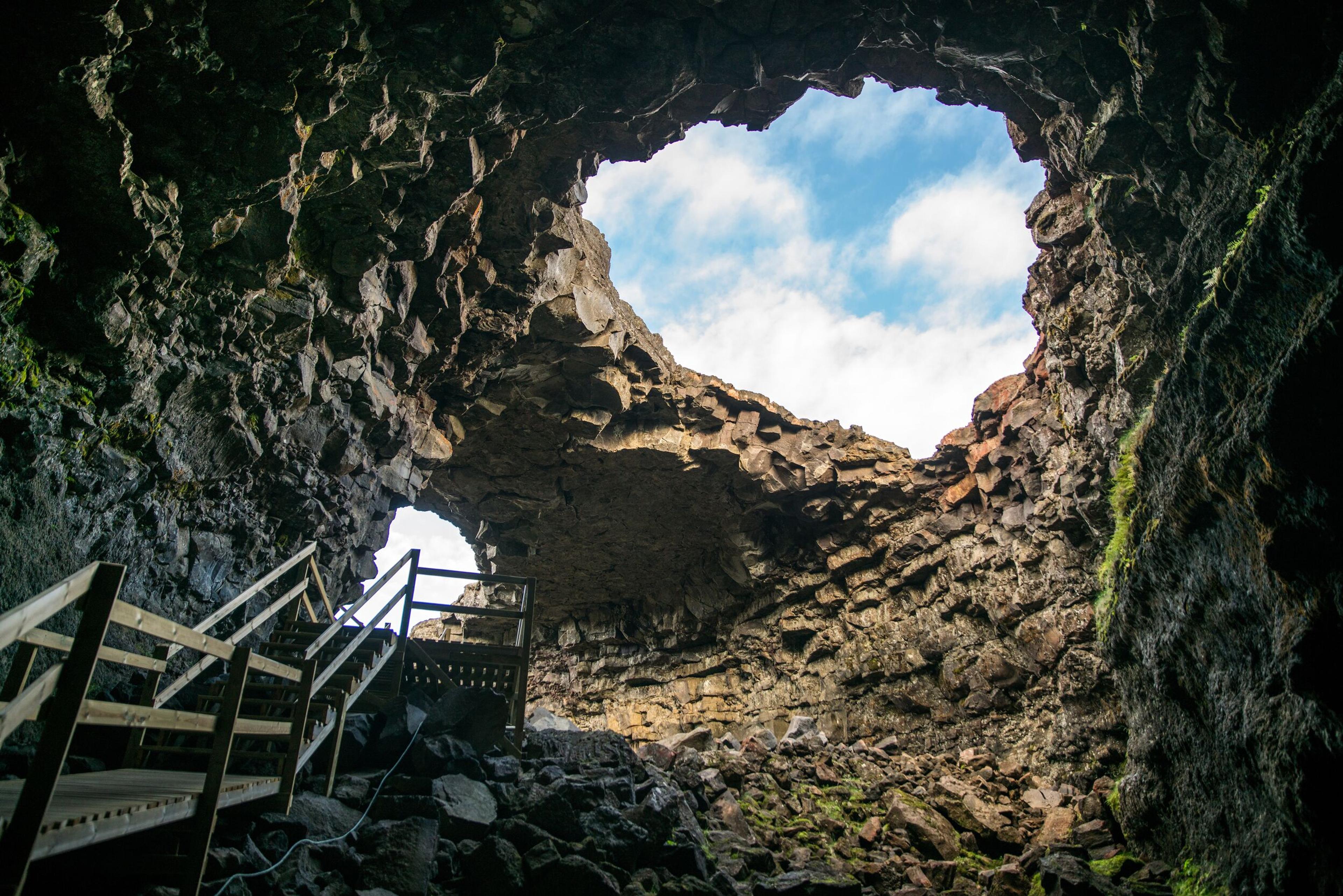 Entrance to a lava cave in Iceland with a wooden pathway leading down into the subterranean depths.