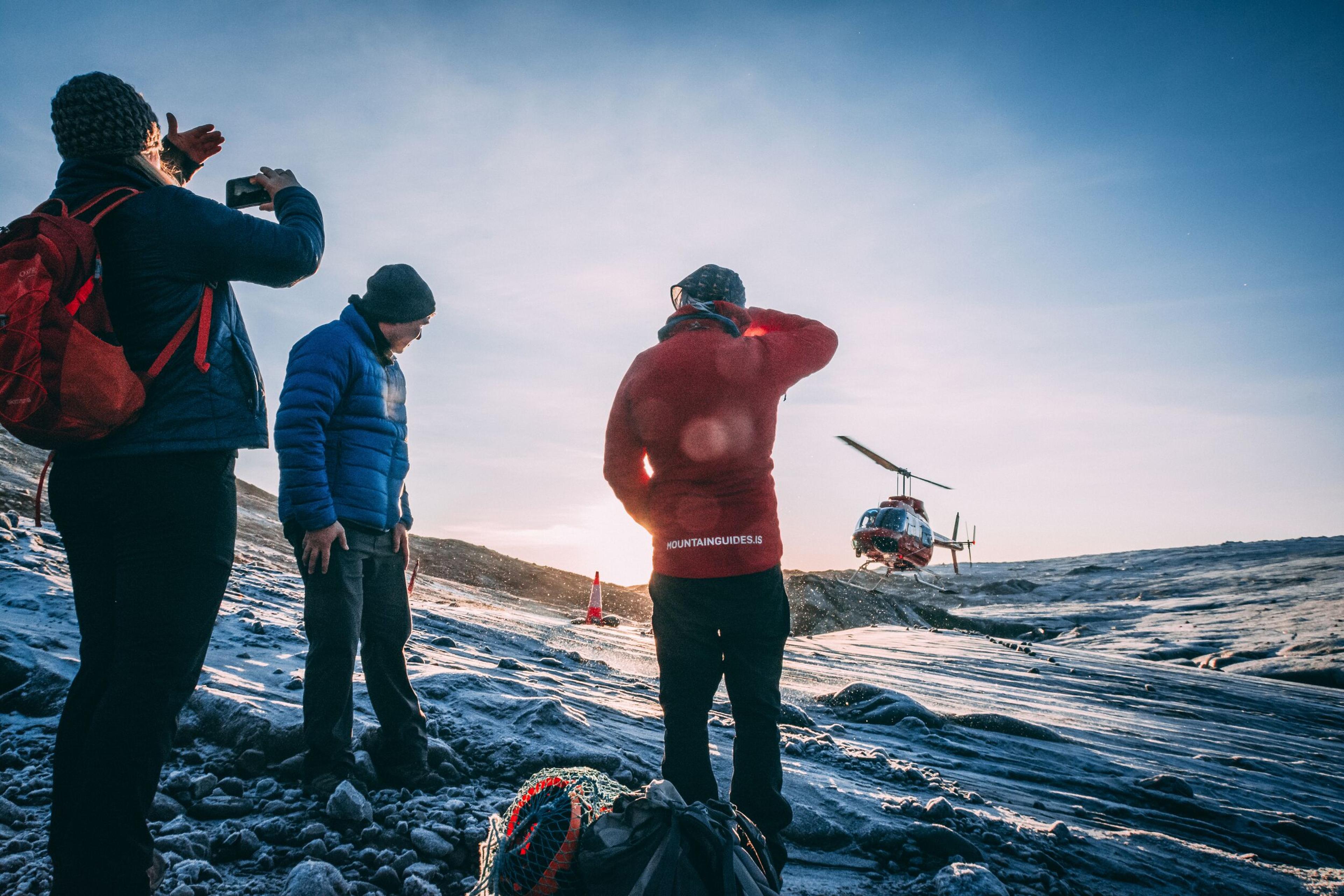 Three men looking at a red helicopter landing on a glacier in Iceland.