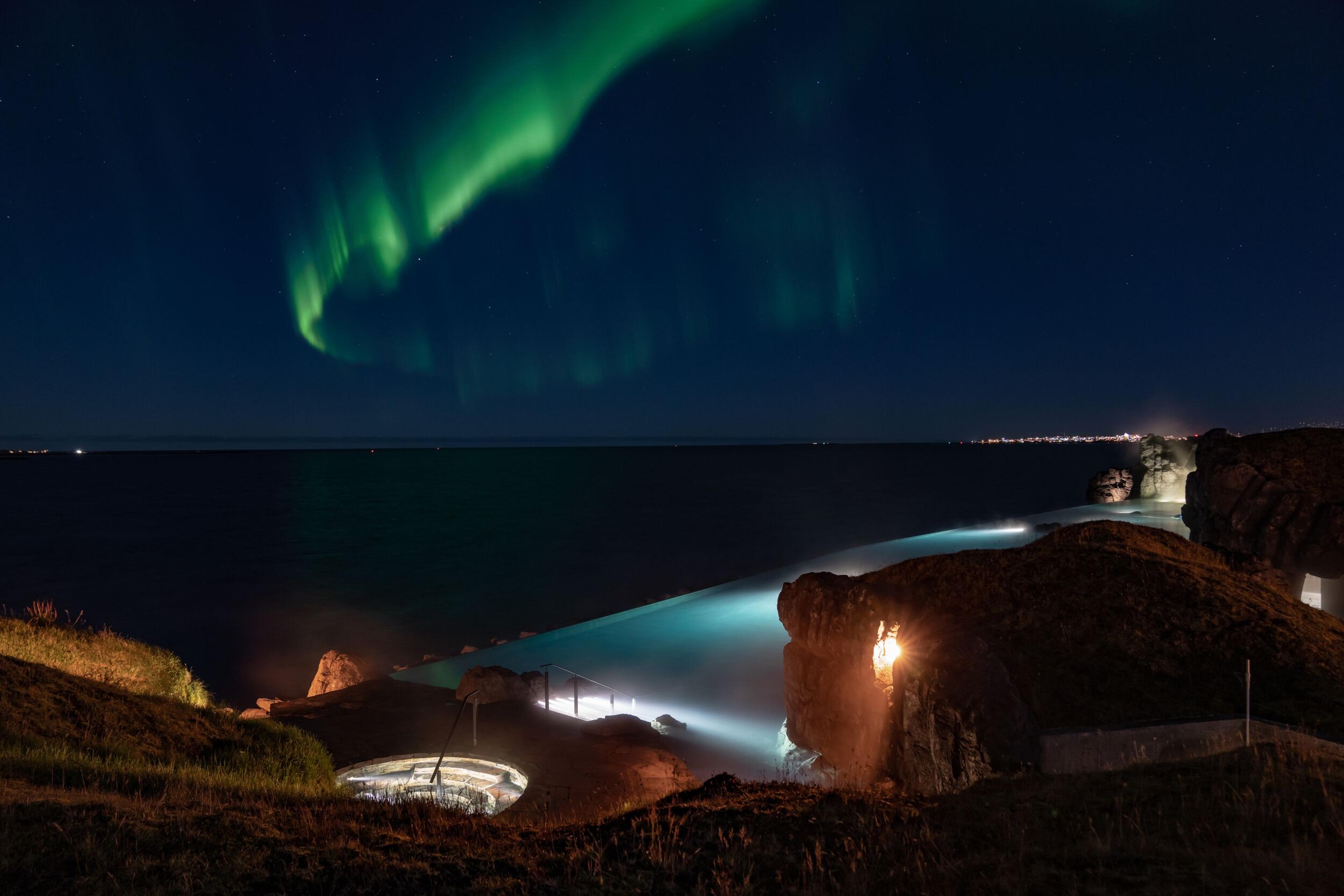 Sky Lagoon in Reykjavík featuring a tranquil infinity pool and natural rocks, with Northern Lights glowing above in the night sky.