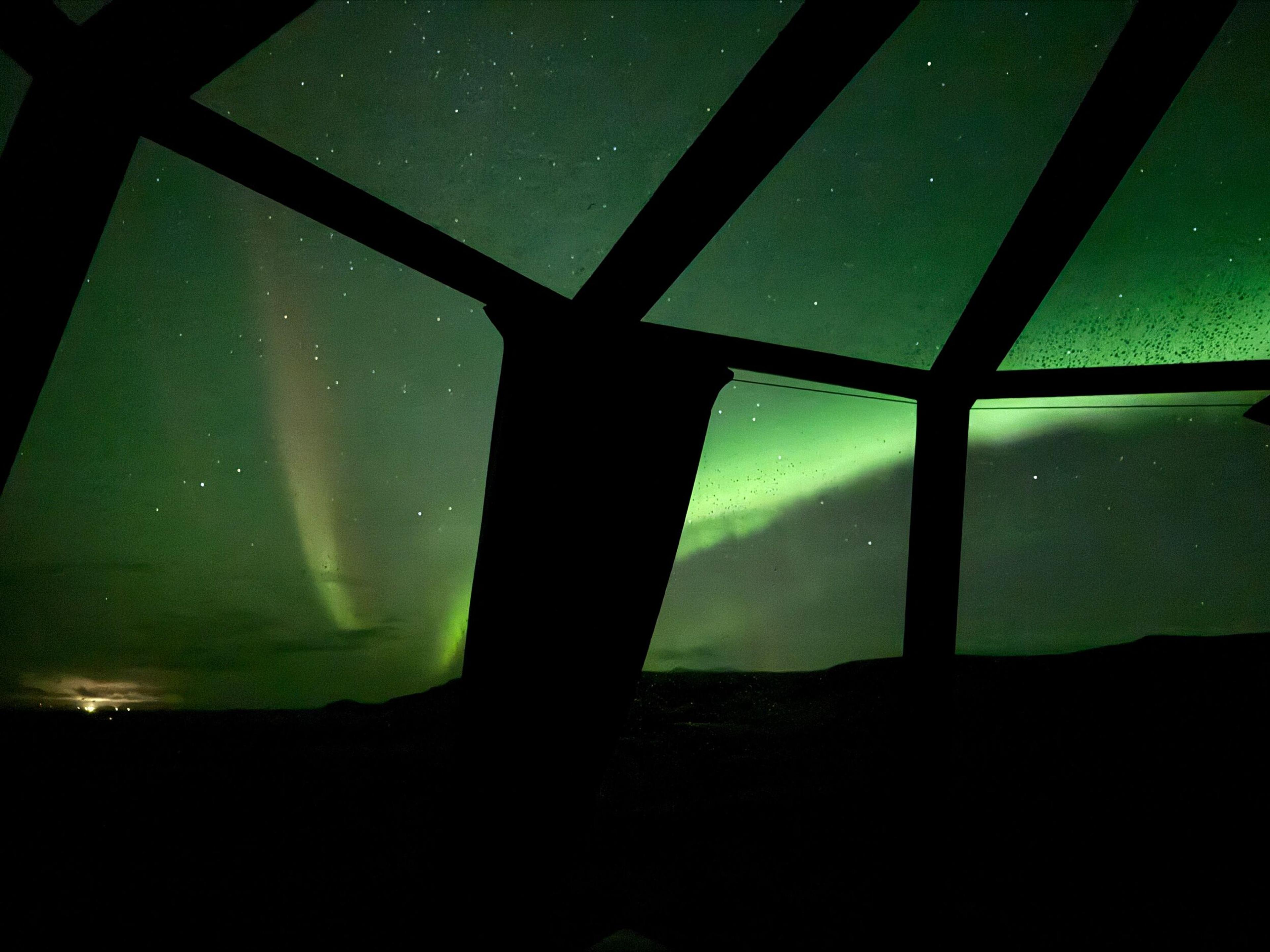 Green Northern Lights visible through dark window frames against a starry night sky.