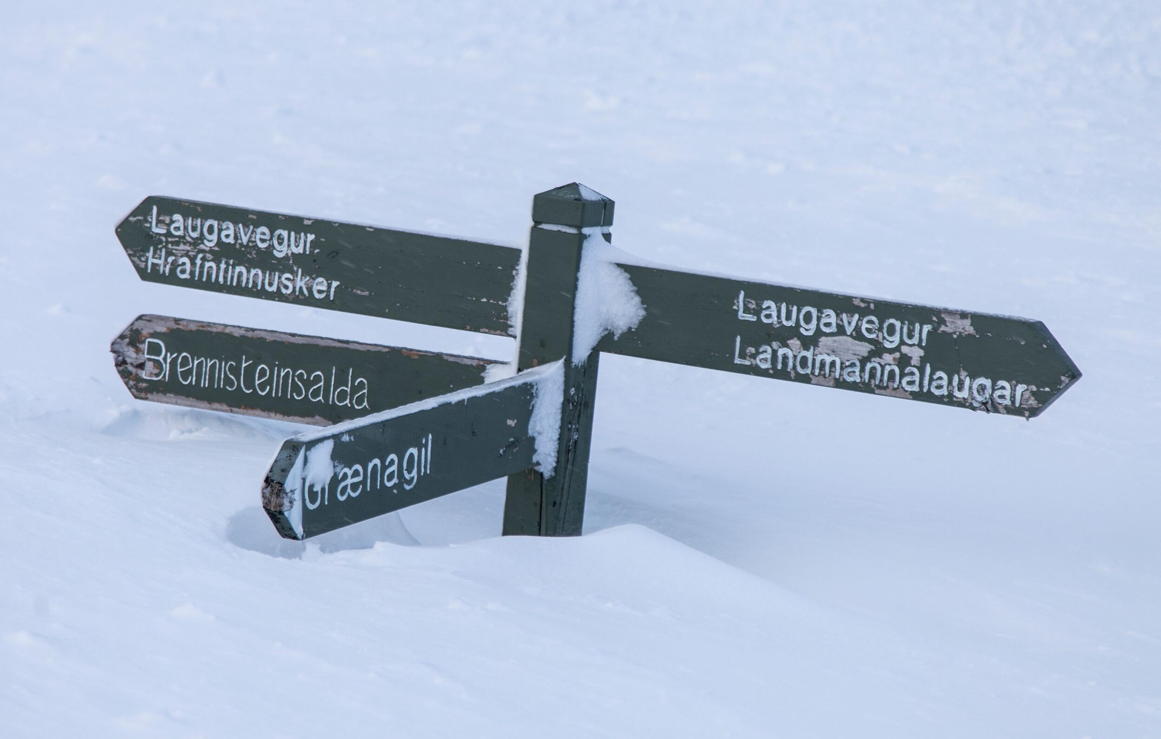 A snow-covered wooden signpost showing hiking trail directions in Landmannalaugar.