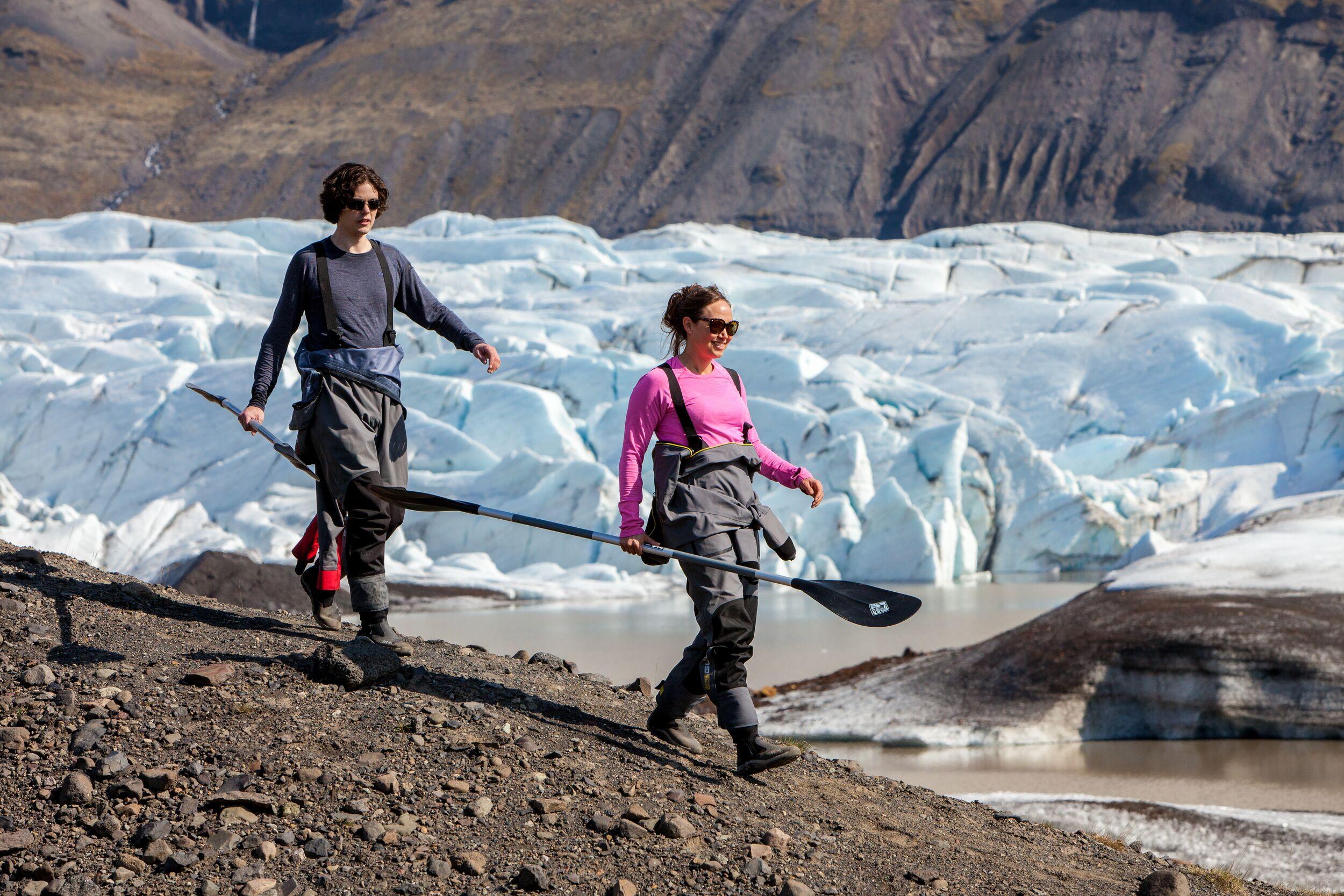 a man and a woman are walking on a rocky hill near a glacier .
