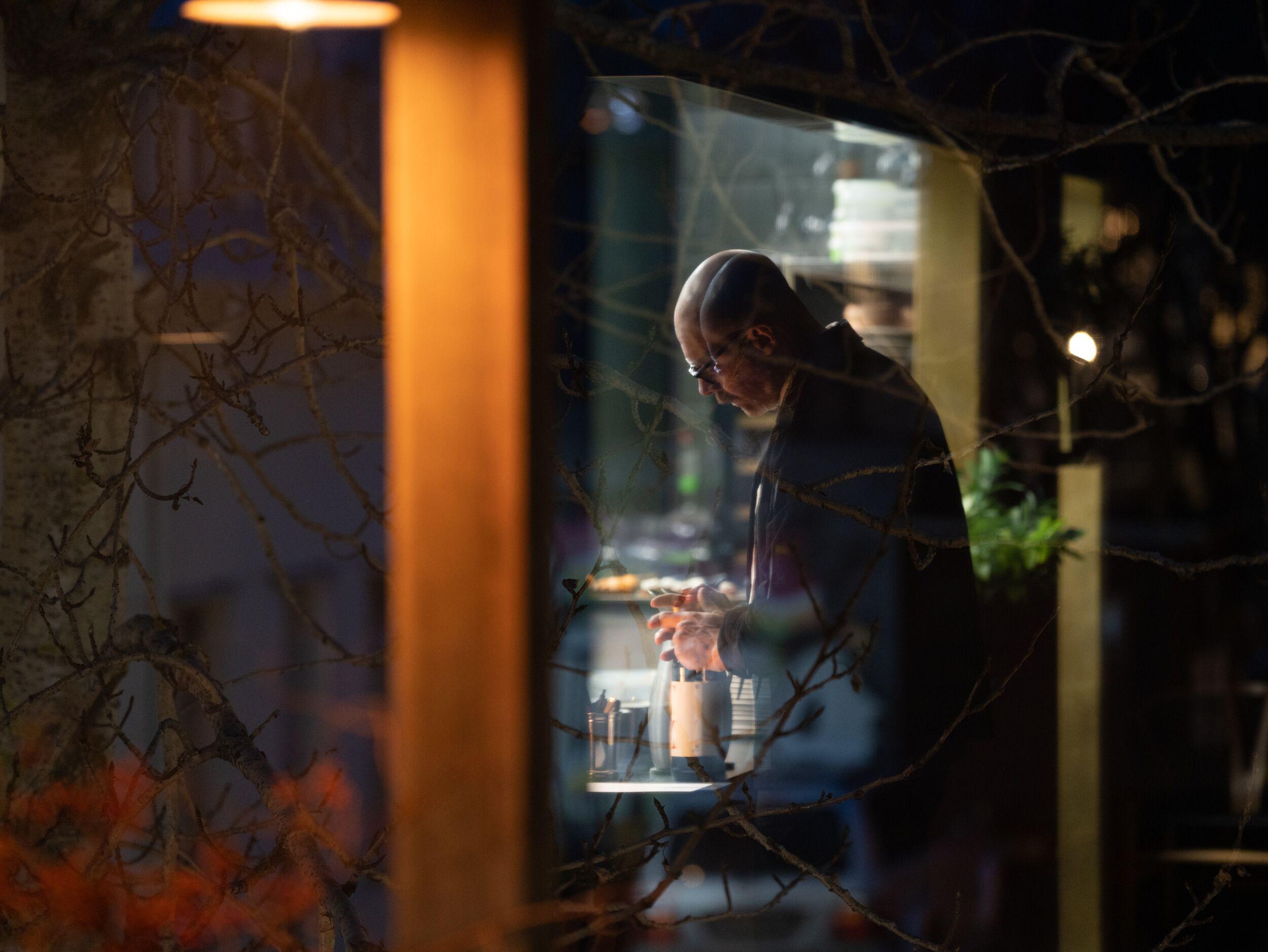 A chef works under bright task lights in a dark kitchen, with soft decorative lanterns hanging above.