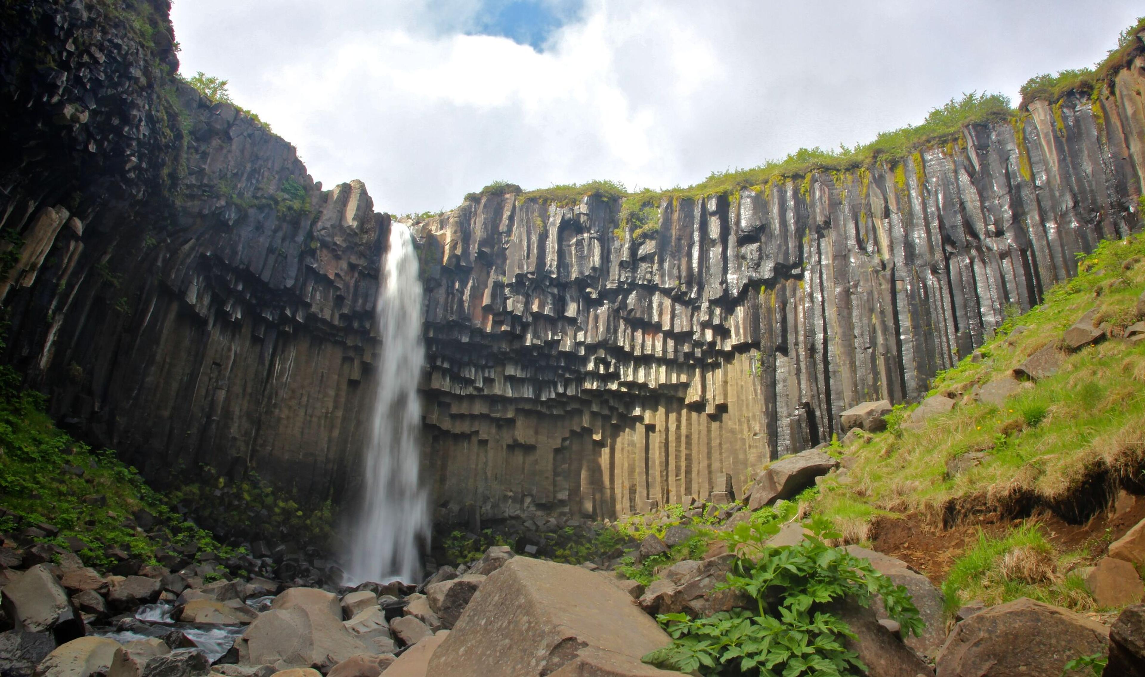 Waterfall framed by tall basalt columns and green vegetation